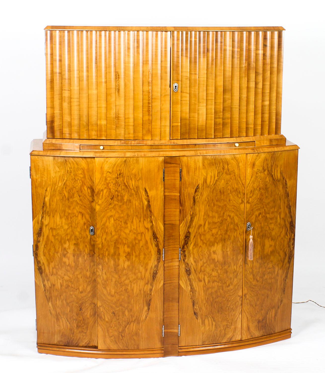 This is a fantastic antique Art Deco burr walnut bow fronted cocktail cabinet, circa 1930 in date and in the manner of Epstein.

This beautiful cabinet's upper part comprises a pair of ripple panelled doors enclosing a striking fitted mirrored