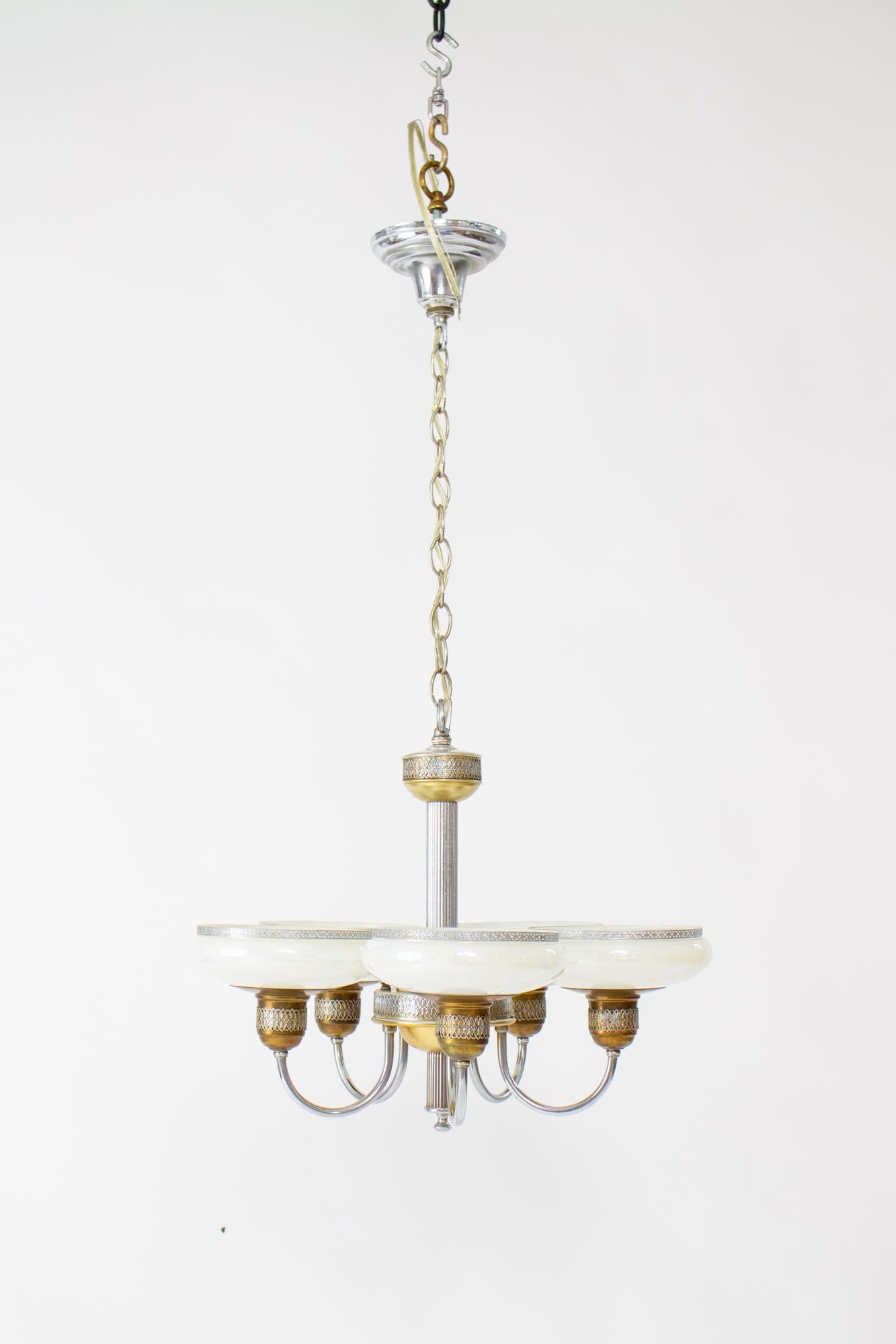 1930’s Art Deco chandelier with iridescent glass and a mixed metal look. The chandelier has a ribbed central stem and five arms that curve up to hold saucer shaped iridescent glass shades. It is designed with a two toned chrome and brass look, and