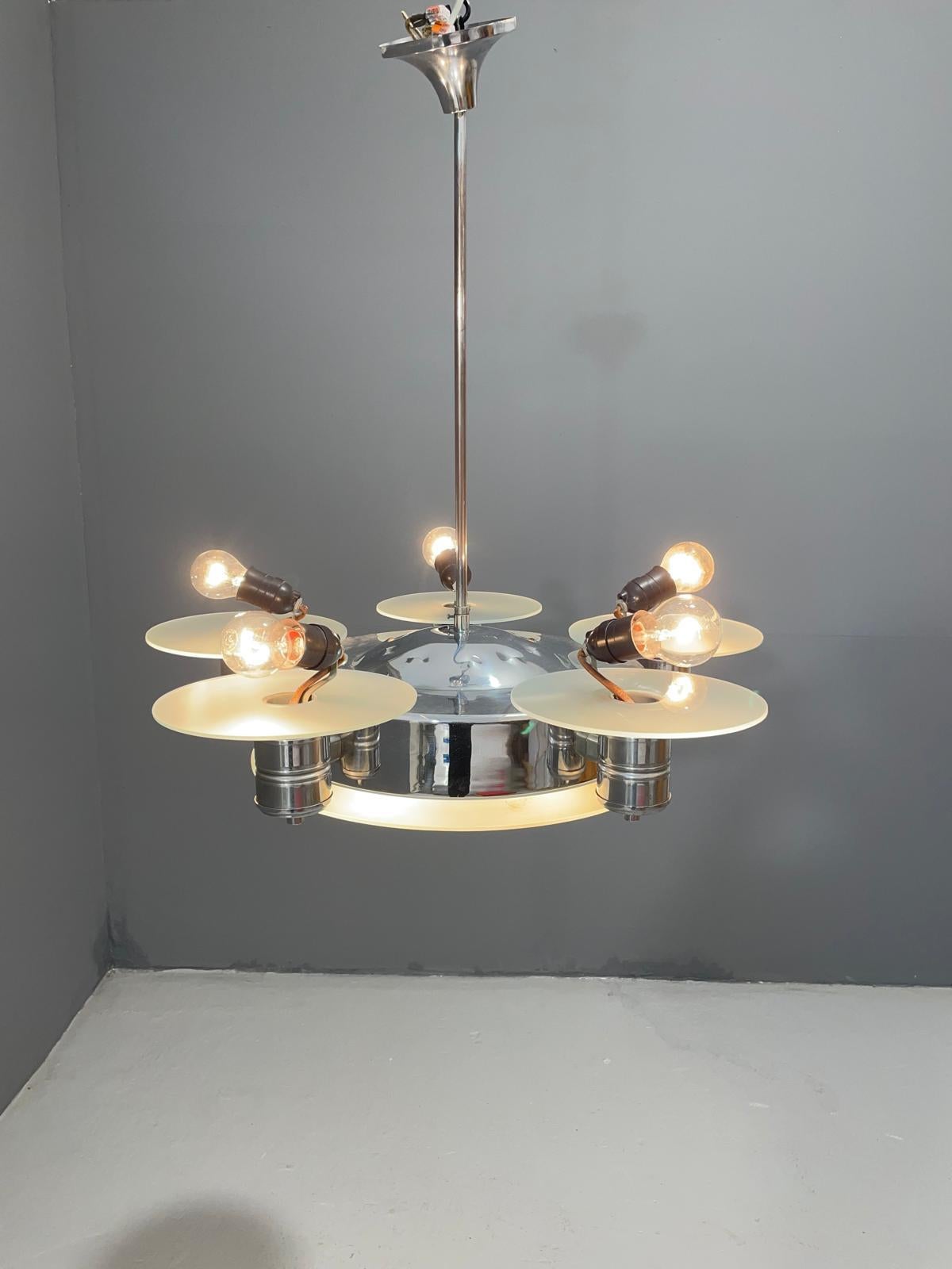Ce remarquable lustre Art déco a été produit dans les années 1930 en Tchécoslovaquie. Elle se compose d'un cadre en métal chromé et de six abat-jour en verre dépoli, disposés de manière circulaire autour d'un bol central en verre. Le verre est