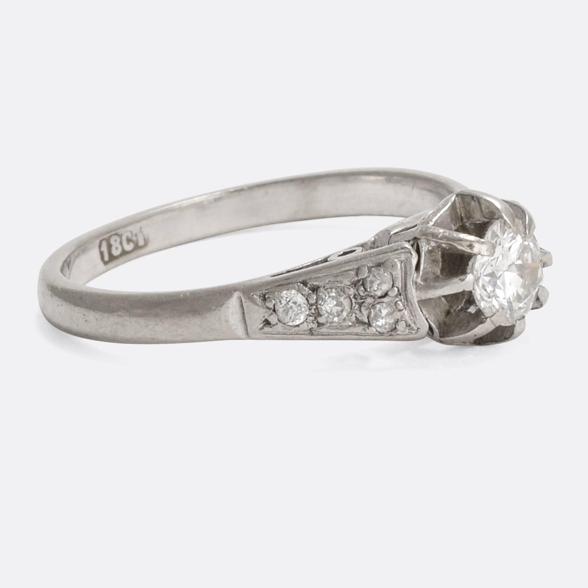 A stylish Art Deco diamond solitaire engagement ring, set with a .40ct old English brilliant cut stone in elegant scalloped mounts. It's modelled in 18 karat white gold, well proportioned with diamond shoulder accents.

STONES
Old English Brilliant