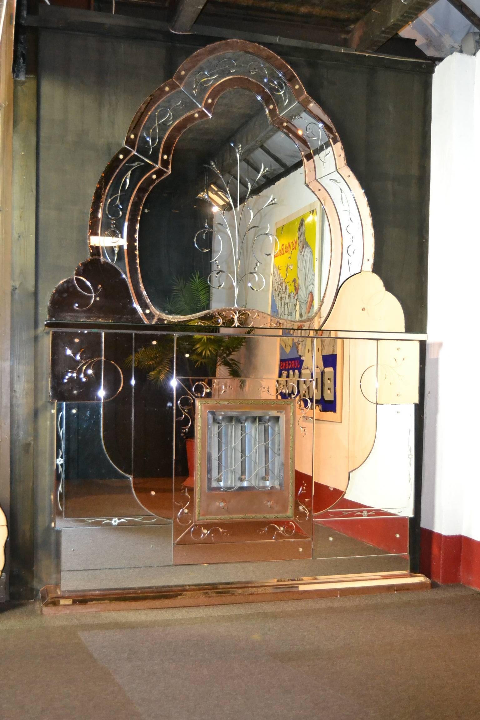 Exklusive große Wanddekoration oder Kunstwerk, dieser elektrische Art Deco-Kamin. 
Ein stilvoller Kamin aus den 1930er Jahren mit einem Heizgerät im Inneren und einem Spiegel über dem Mantel. 
Es ist aus zweifarbigem, abgeschrägtem Spiegelglas