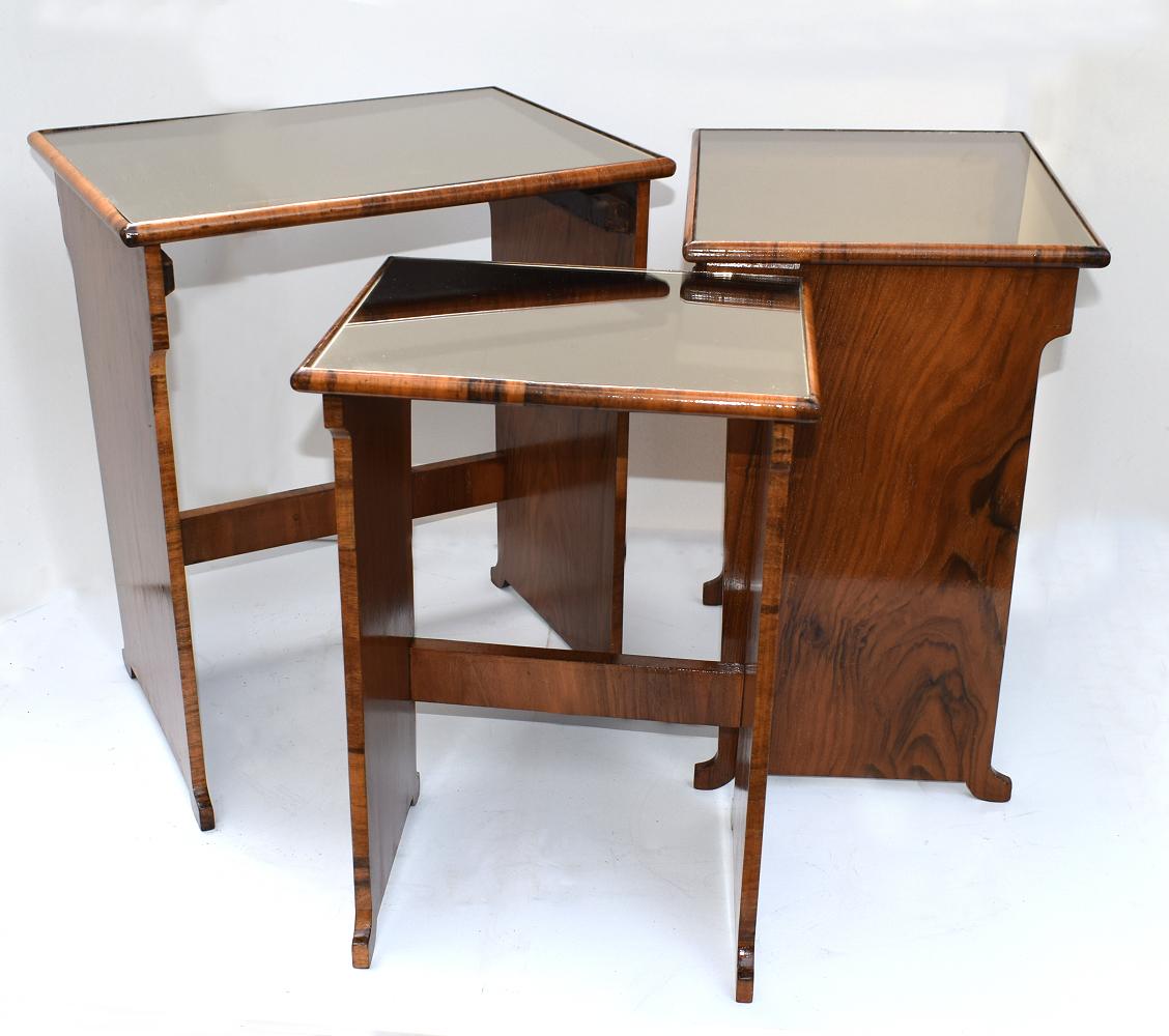 A stylish 1930s Art Deco nest of tables originating from England. One large table with two under tier insert tables with the most exquisite warm walnut veneers and colored mirrored tops. A rare classic set to enhance your home interior. In excellent