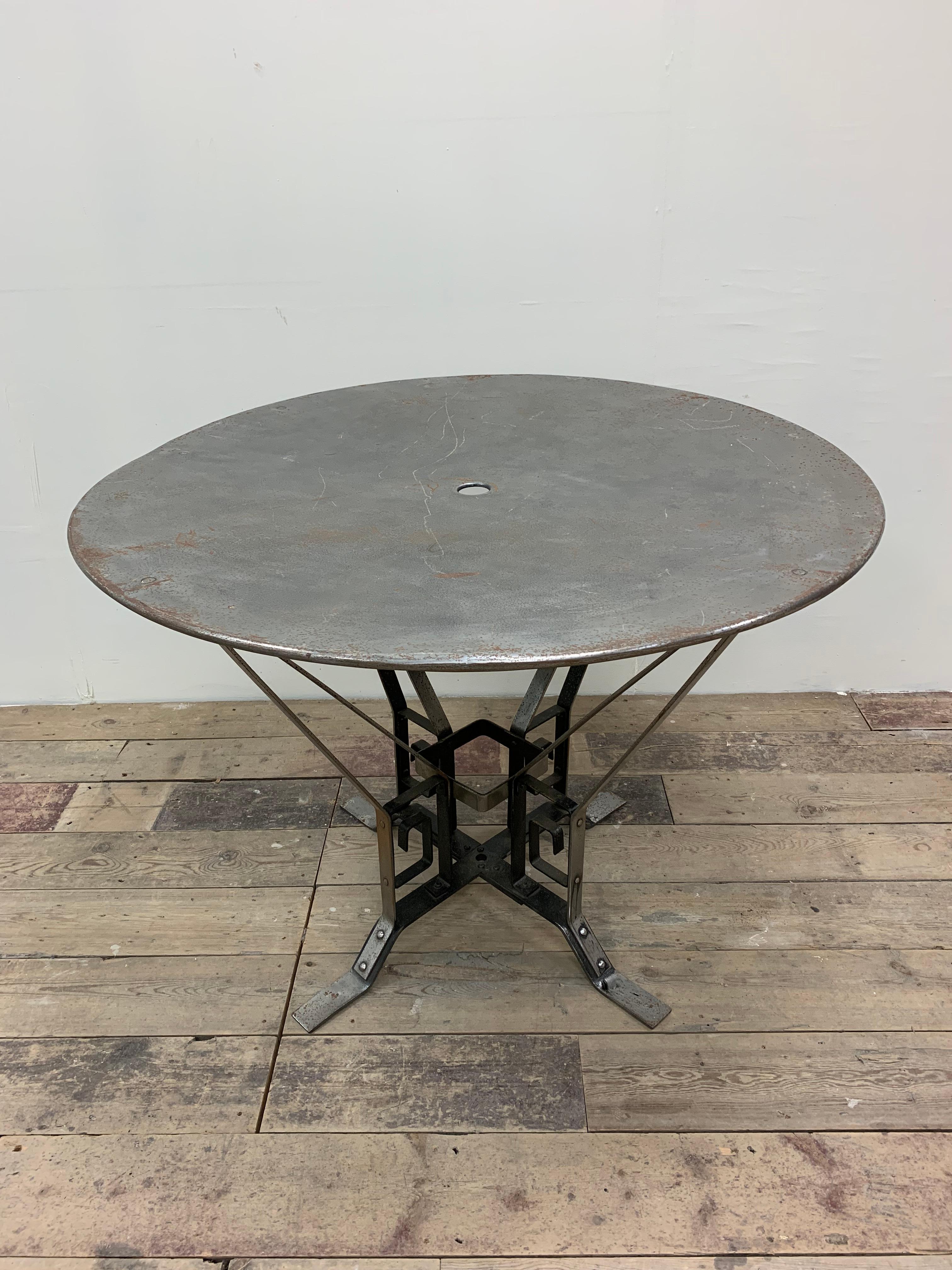 A French industrial round metal garden or conservatory table illustrating the early influence of Art Deco.  The base is constructed from polished wrought iron which has been riveted together, the rivets being a feature.  The extended flat legs allow