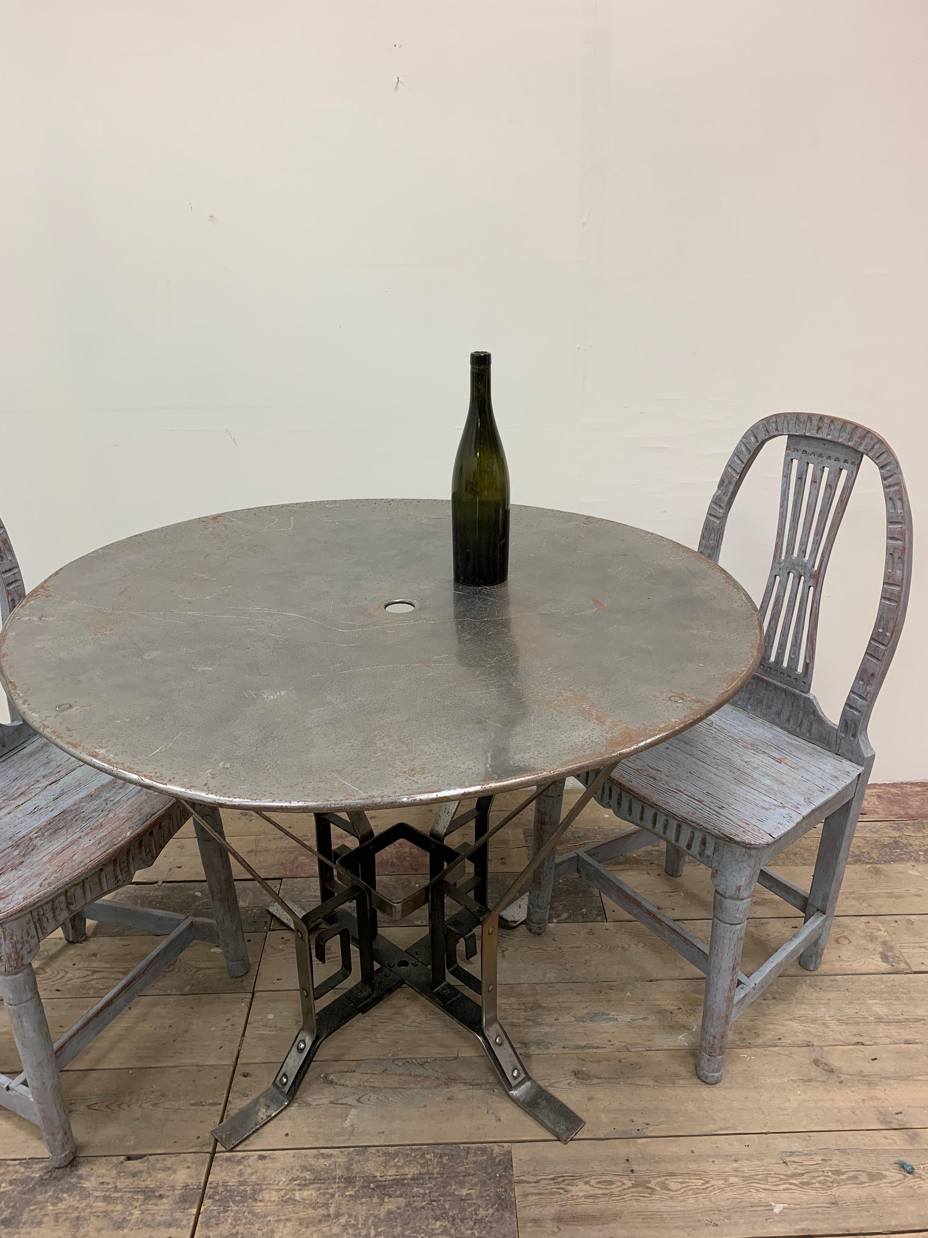 A french industrial round metal garden or conservatory table illustrating the early influence of Art Deco.
The base is is constructed from polished wrought iron which has been riveted  together, the rivets being a feature. 
The extended flat legs