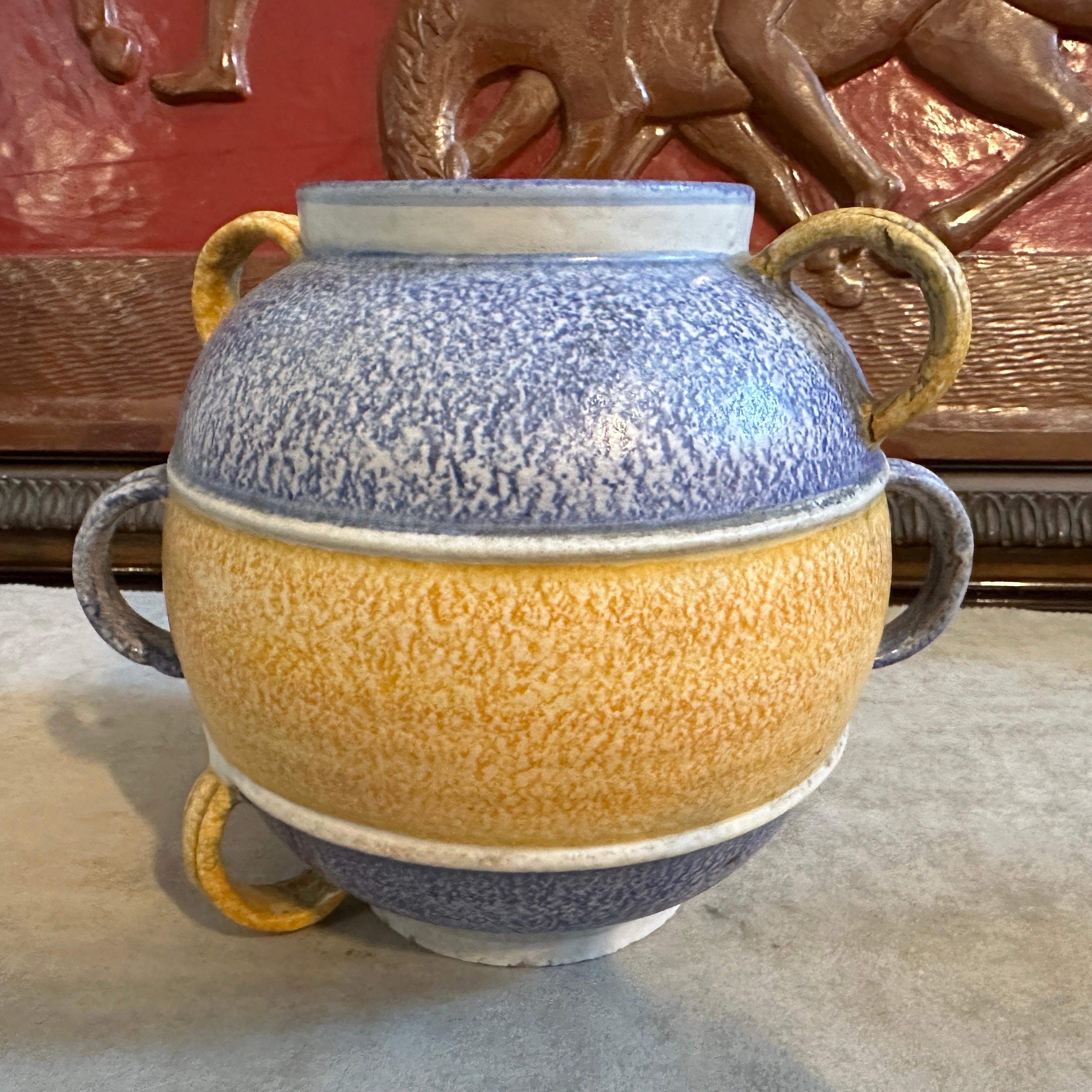 Ce vase est un magnifique mélange de design géométrique, de textures riches et de couleurs vibrantes. La céramique polychrome présente un schéma de couleurs en couches : des bandes de bleu et de jaune d'or dominent la pièce, divisée en sections