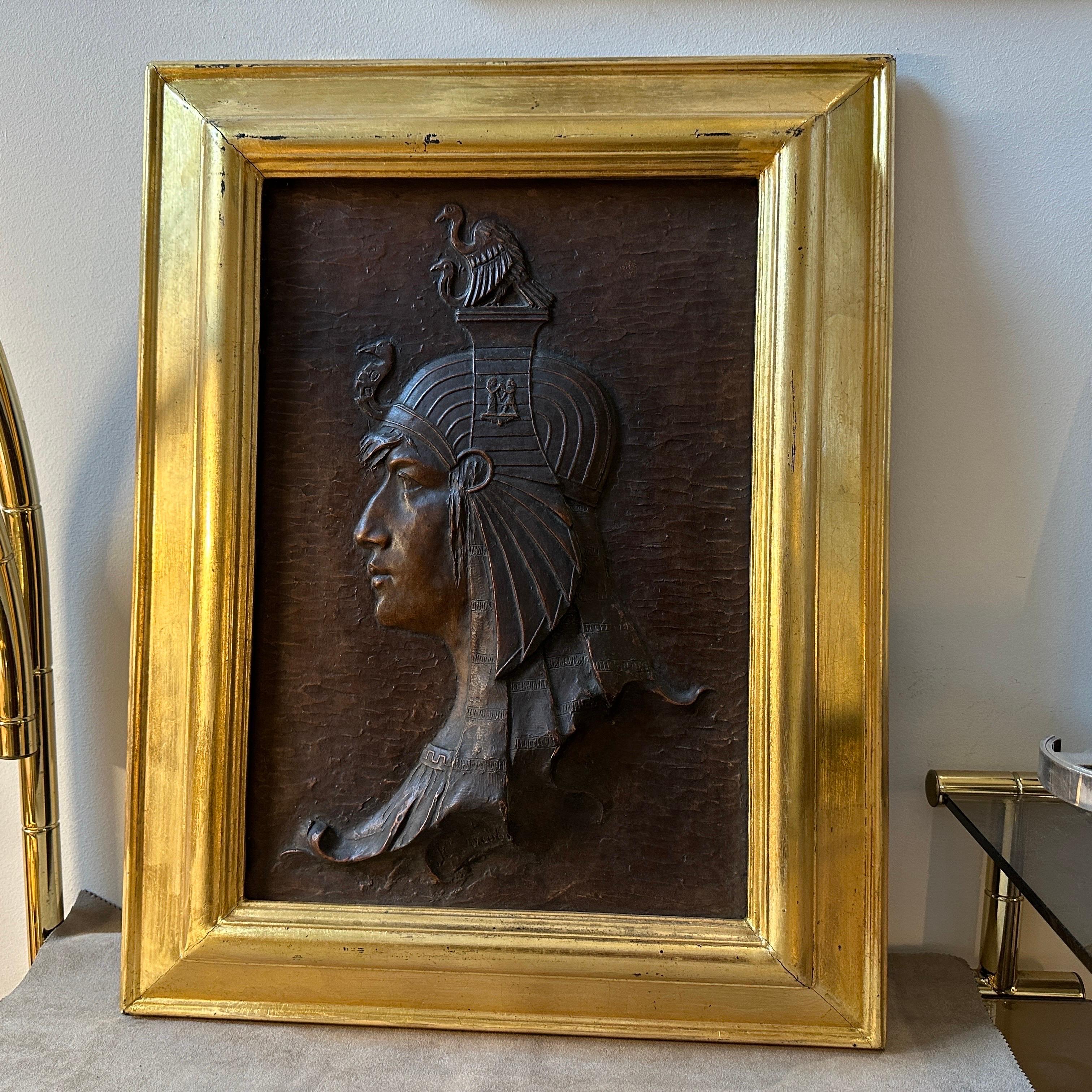 An Art Deco gilded wood framed Bas-Relief Plaster depicting an antique Egyptian hand-crafted in Italy in the Thirties which represents a stunning fusion of artistic influences and craftsmanship from the early 20th century. This particular piece