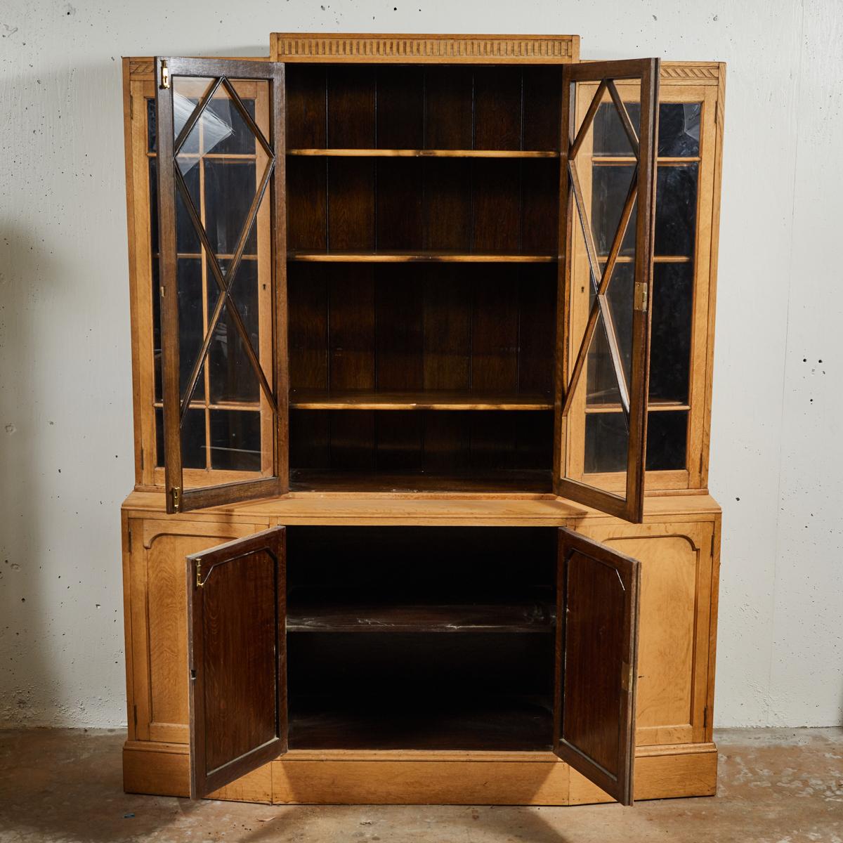 Art Deco blonde oak bookcase, cabinet, or vitrine from the 1930s, designed by distinguished English furniture maker Heals. The handsome breakfront top is surmounted by a carved frieze with dentil molding, and provides ample room for storage and