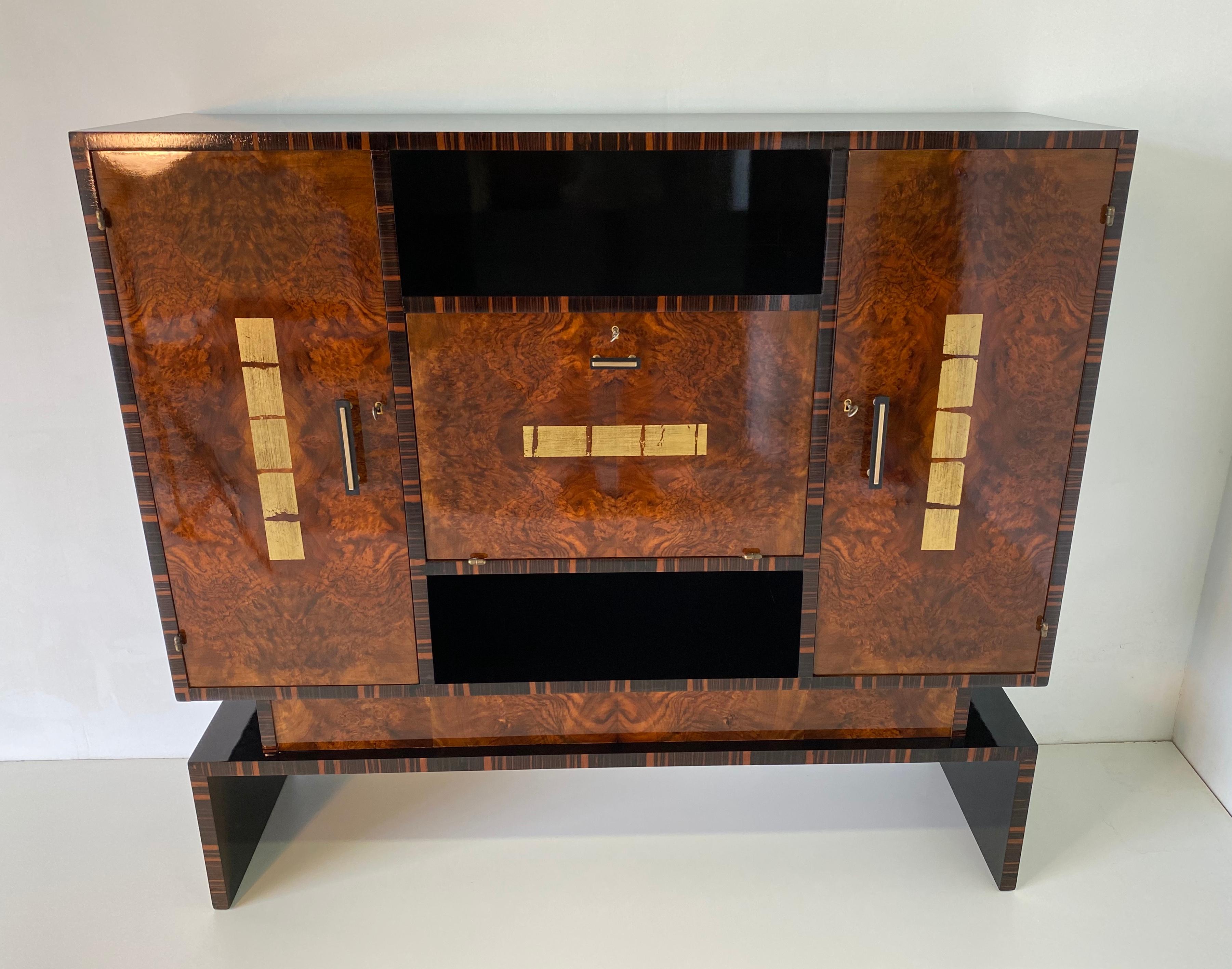 This rare cabinet was produced in Italy in the 1930s.
The structure is black lacquered while the profiles are in Macassar and the doors are in precious walnut briar.
Decorations on the doors are in gold leaf, the handles are in bakelite and