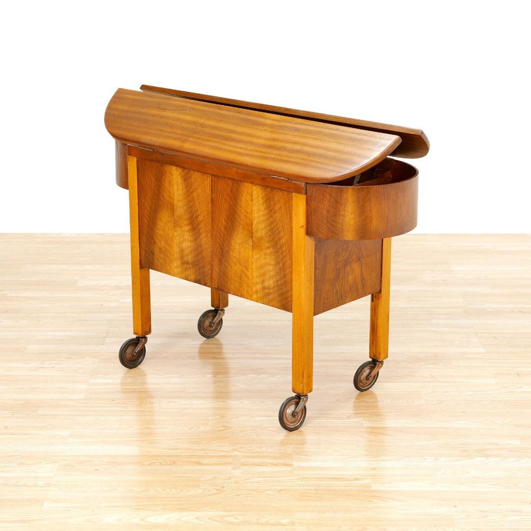 This fantastic Art Deco bar cart was manufactured in England during the 1930s by Besway. Produced in striking English Walnut and Mahogany by Besway, this stunning 'wagon' bar cart was distributed by London department stores such as Harrords and