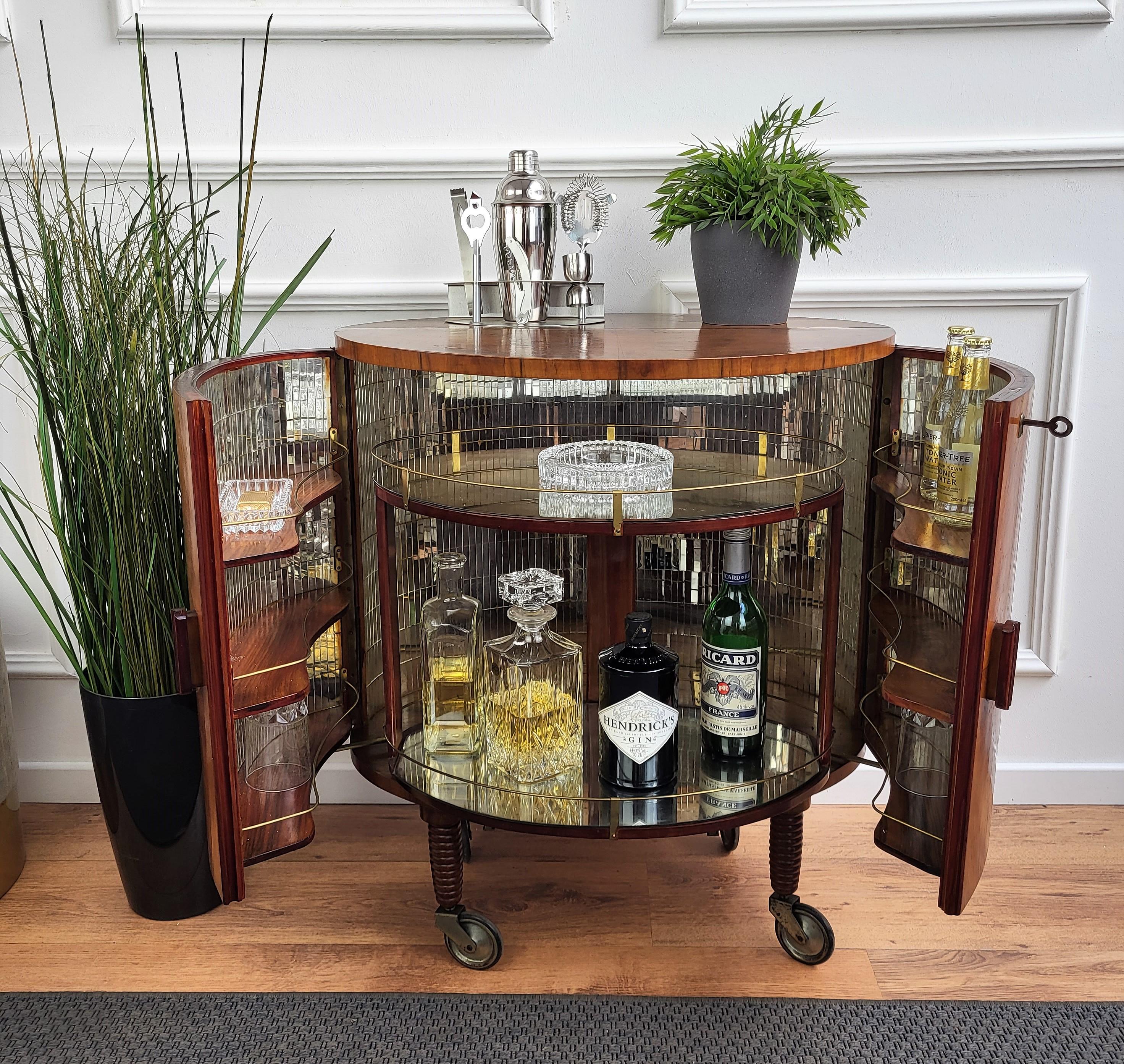 Unique and very elegant Italian Art Deco oval shaped dry bar cabinet cart, in walnut with double front door having amazing interior part in mirrors mosaic and a two-tier central bottle holder that is sliding out to the front when the two doors are