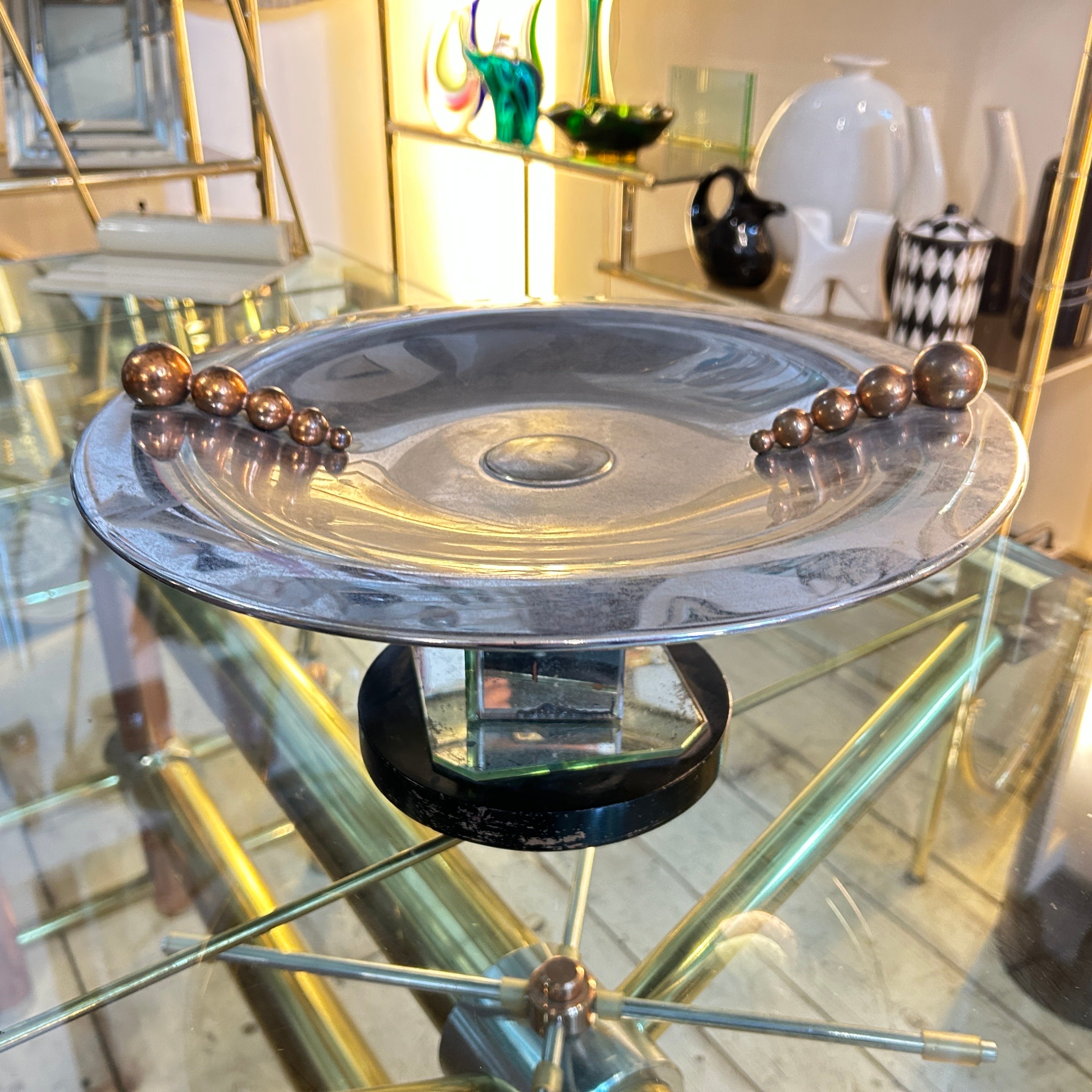 The 1930s Art Deco mirror glass and chromed metal italian round centerpiece stand is a vintage decorative piece that was likely designed in Italy during the Art Deco era of the 1930s. It features a round metal surface supported by a wood and mirror