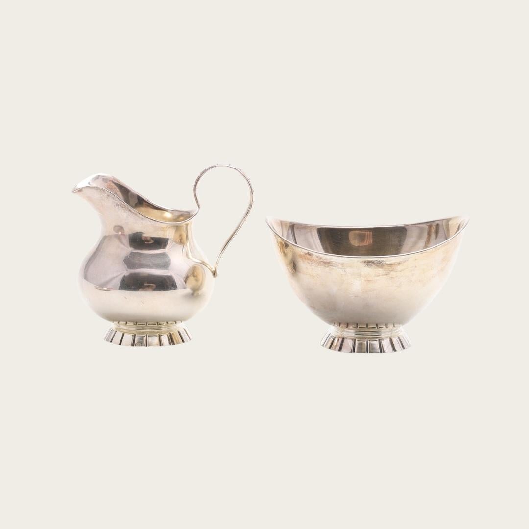 Cet ensemble trois pièces Art déco des années 1930 comprend un sucrier, un verseur à lait et un plateau en maillechort. Chaque pièce présente d'élégants détails gravés linéaires le long des bases et du périmètre du plateau, reflétant le style épuré