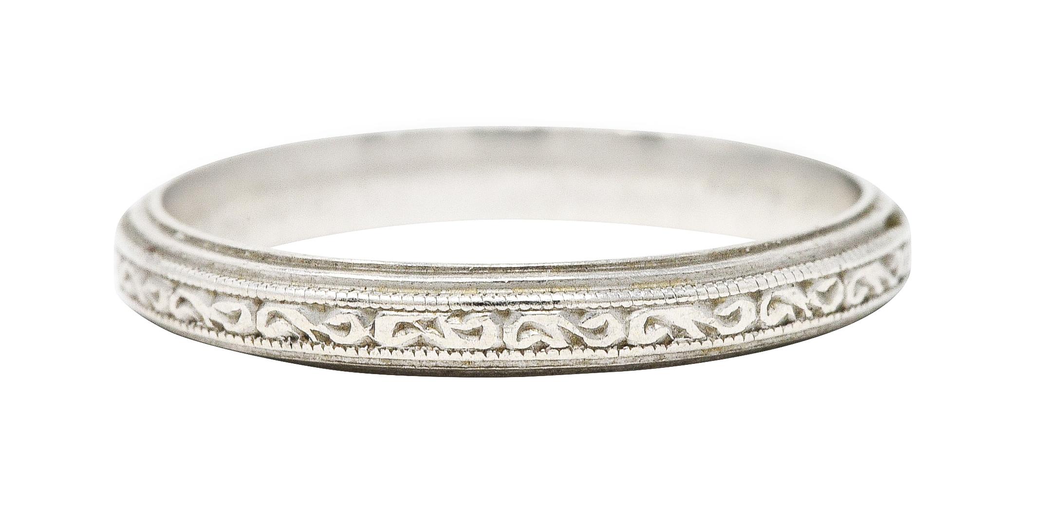 Band ring features engraved scroll motif fully around. With grooved edges. Stamped for platinum. Circa: 1930's. Ring size: 6 1/4 and not sizable. Measures: North to South 2.5 mm and sits 1.5 mm high. Total weight: 3.1 grams. Swirling. Intricate.