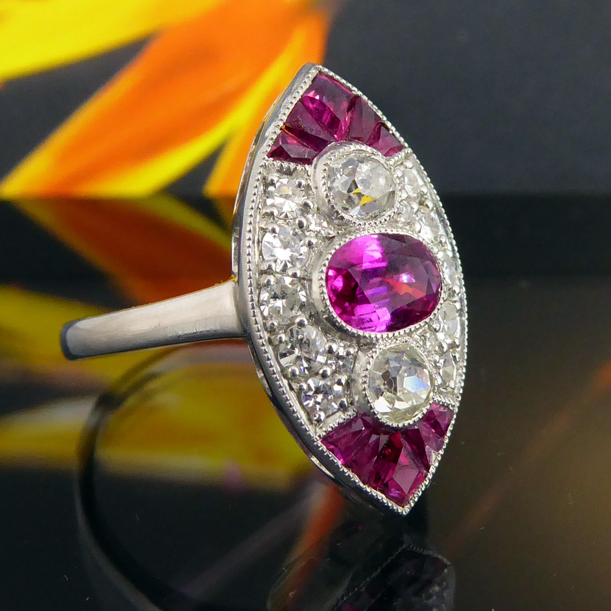 A beautiful ruby and diamond ring from the Art Deco era in a cluster style.  Centring on a millegrain set, oval mixed cut, medium colour ruby approx. 0.66ct and measuring 6.00mm x 4.30mm x 2.57mm.  The ruby is flanked to the top and bottom by an old