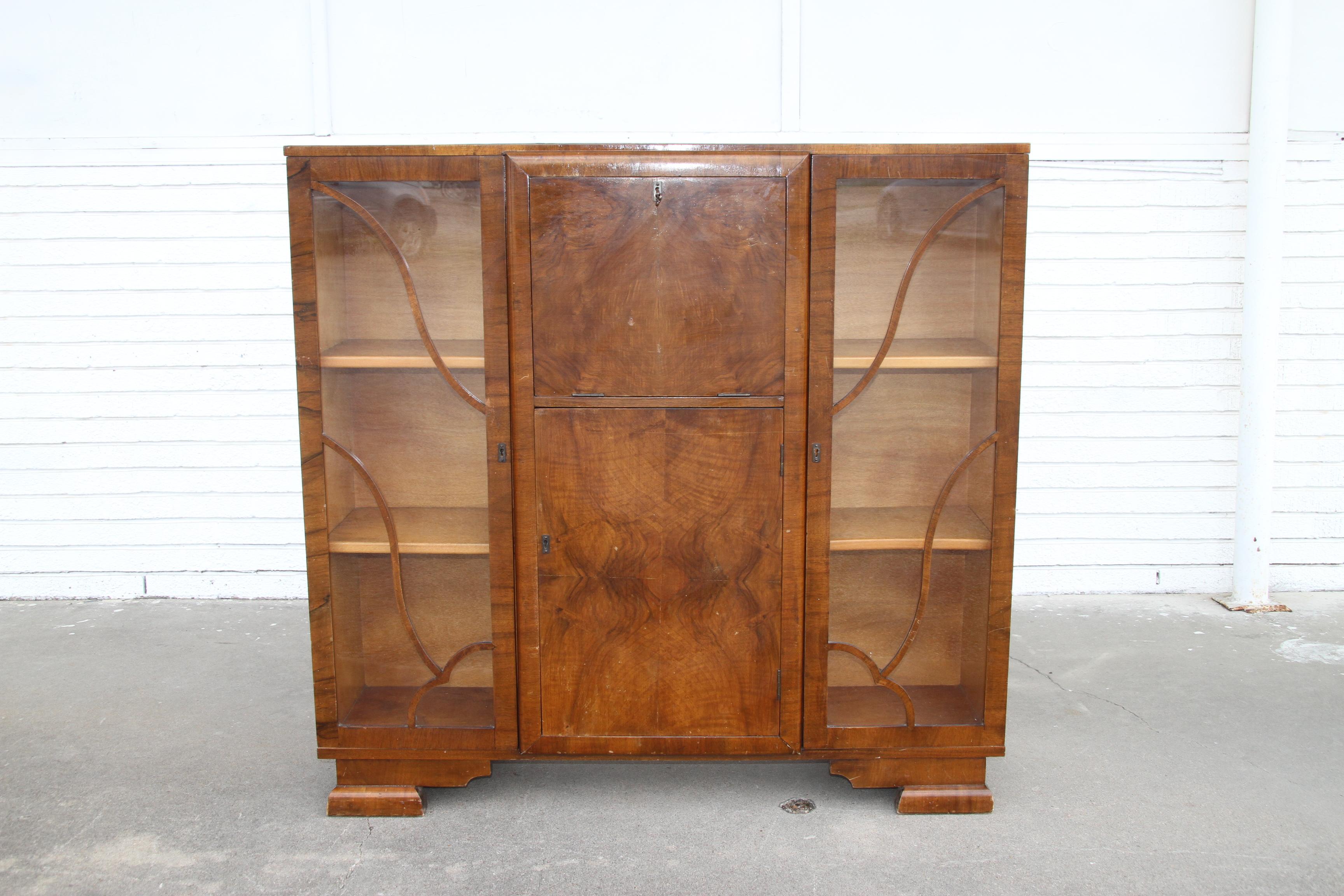 1930s Art Deco secretary cabinet.

Exquisite Art Deco display cabinet in walnut with glass front doors featuring fretwork design. The center features a drop down work surface secretary and pidgeon hole compartments. Includes lower cabinet for