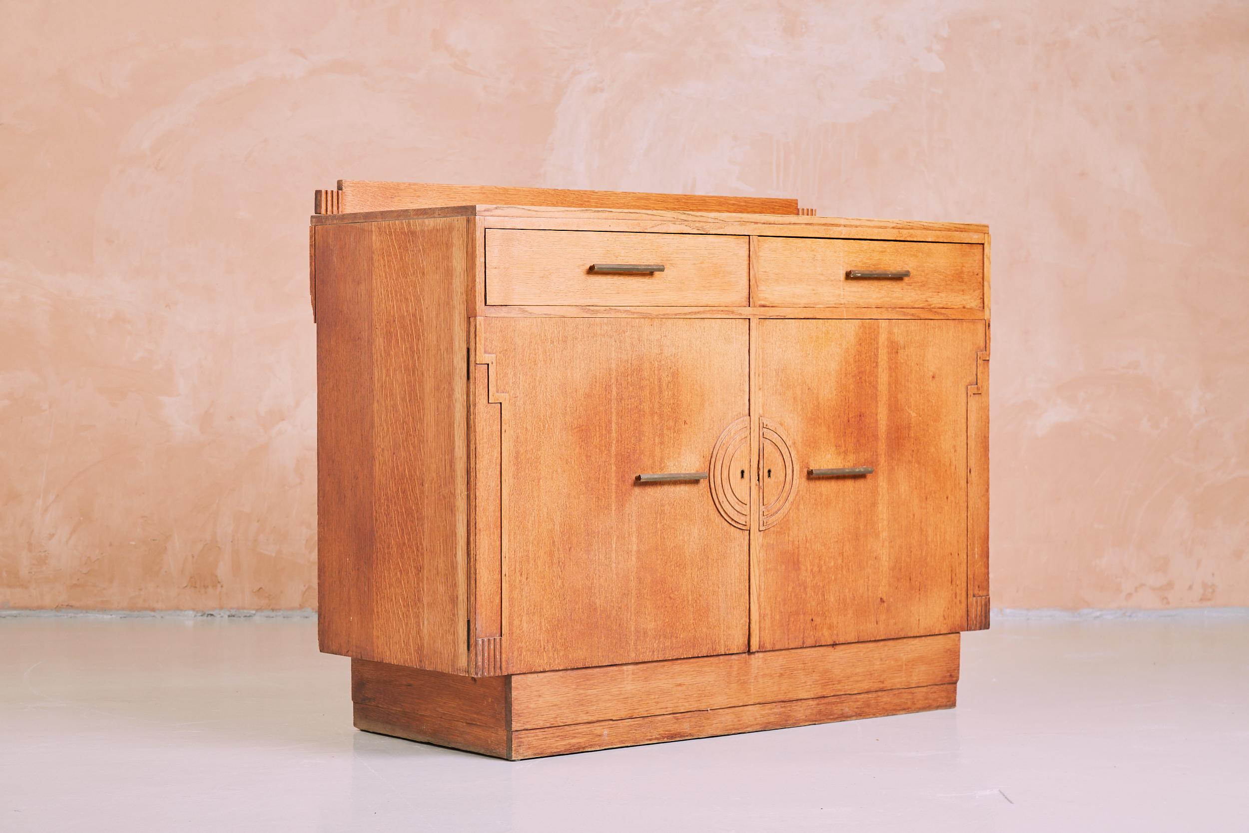An Art Deco sideboard constructed in solid oak from circa 1930. A rare piece from an era of cabinet making that combined craftsmanship with elegant design. A minimal Art Deco aesthetic with quintessential accents on the cupboard doors, on the rear
