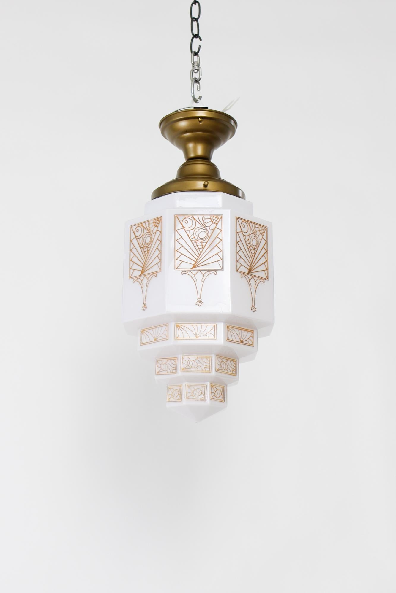 Flush mount fixture in an Antique brass finish. Milk glass in a geometric skyscraper shape with an art deco patterned transfer design in amber. Single Edison base bulb, 100 W max. US 120V. Hardwired. Fixture is new, glass in very good condition for