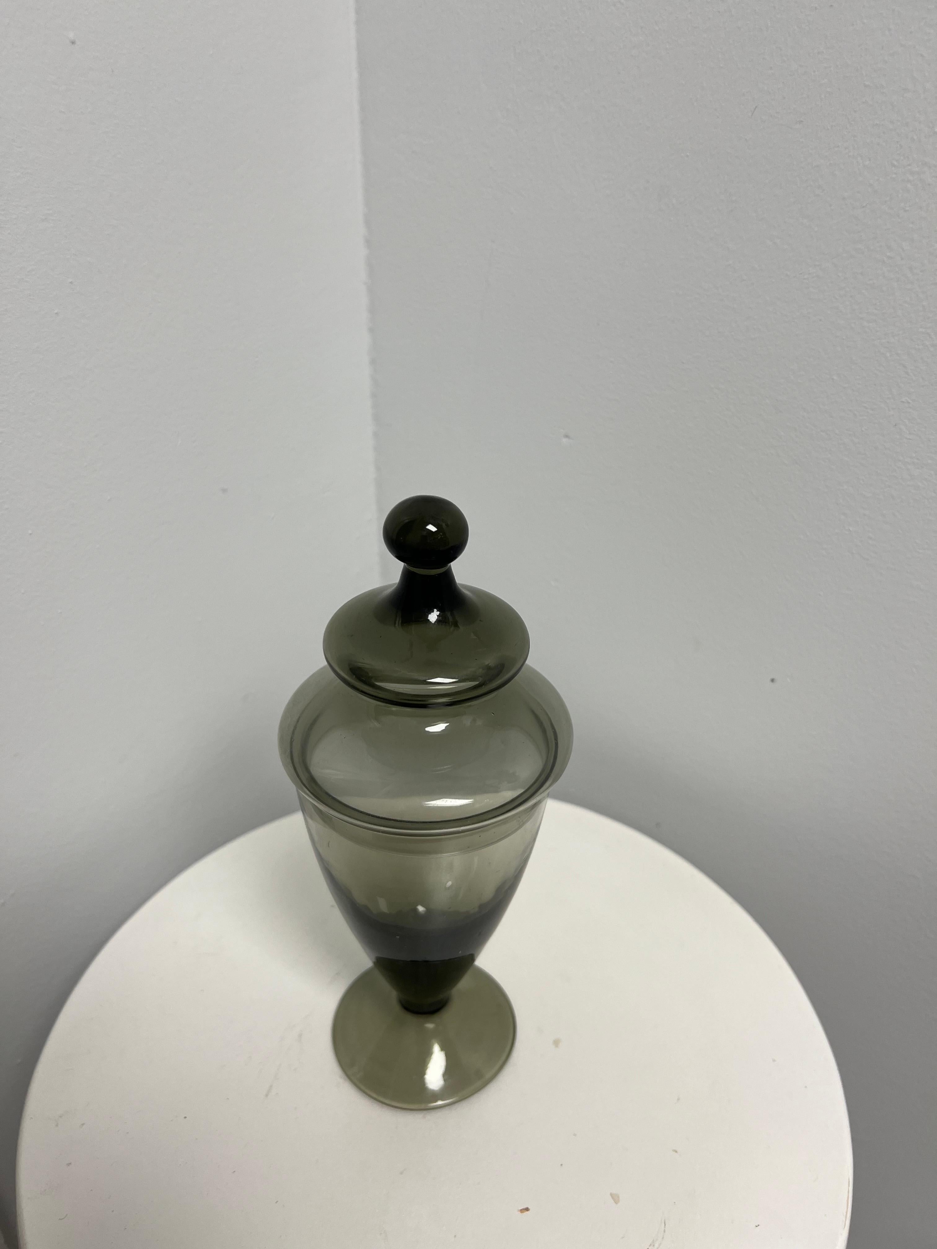 A beautiful smoked gray glass apothecary jar with lid. 

This vintage apothecary jar is a charming addition to any collection. Made in the art deco style, it features a beautiful charcoal gray color and stands at 9.5 inches tall with a width of 4