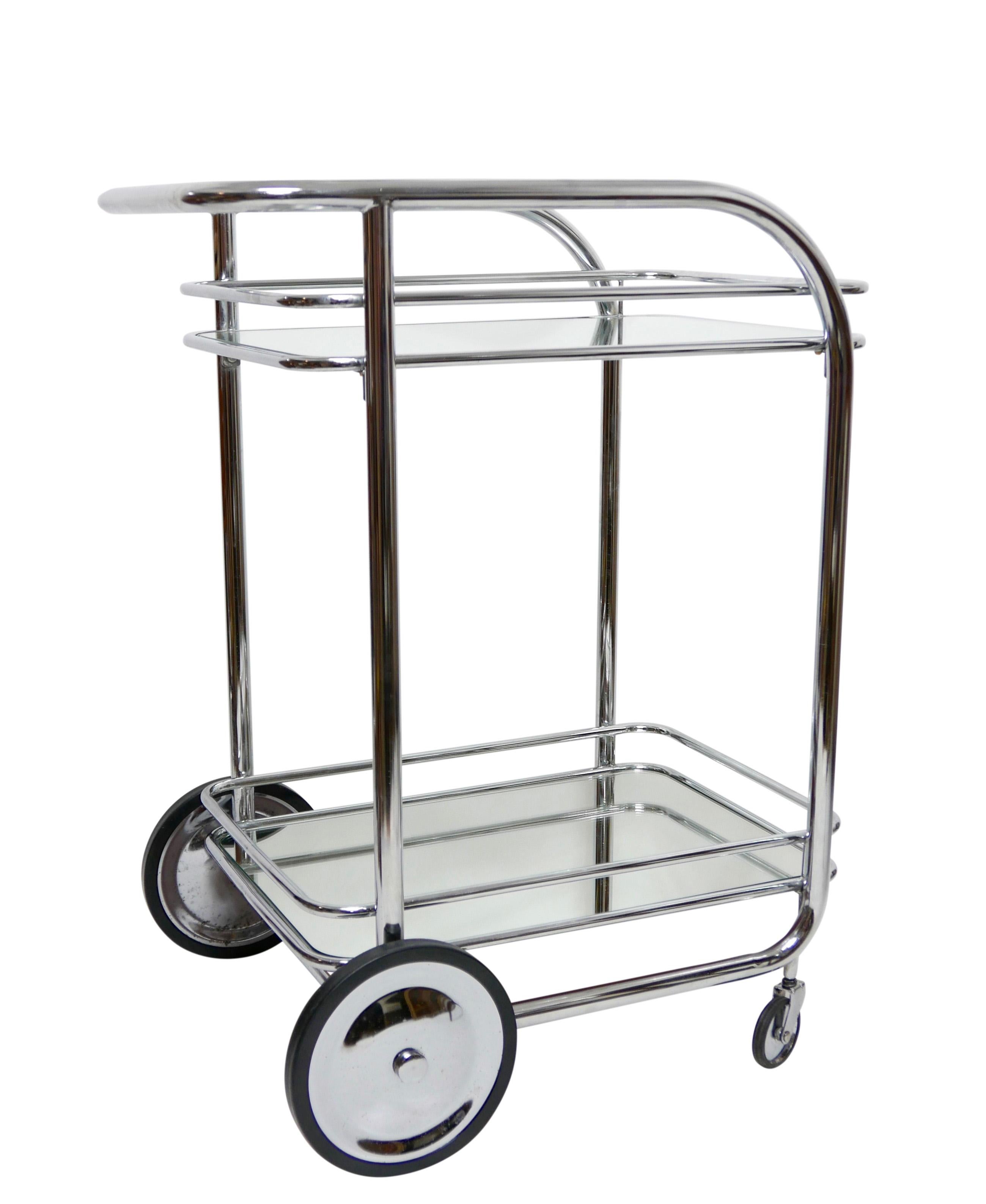 Stylish streamline modern two tier rolling chrome bar cart with top shelf of glass and lower shelf with an inset mirror.,
circa 1930s.
   
  