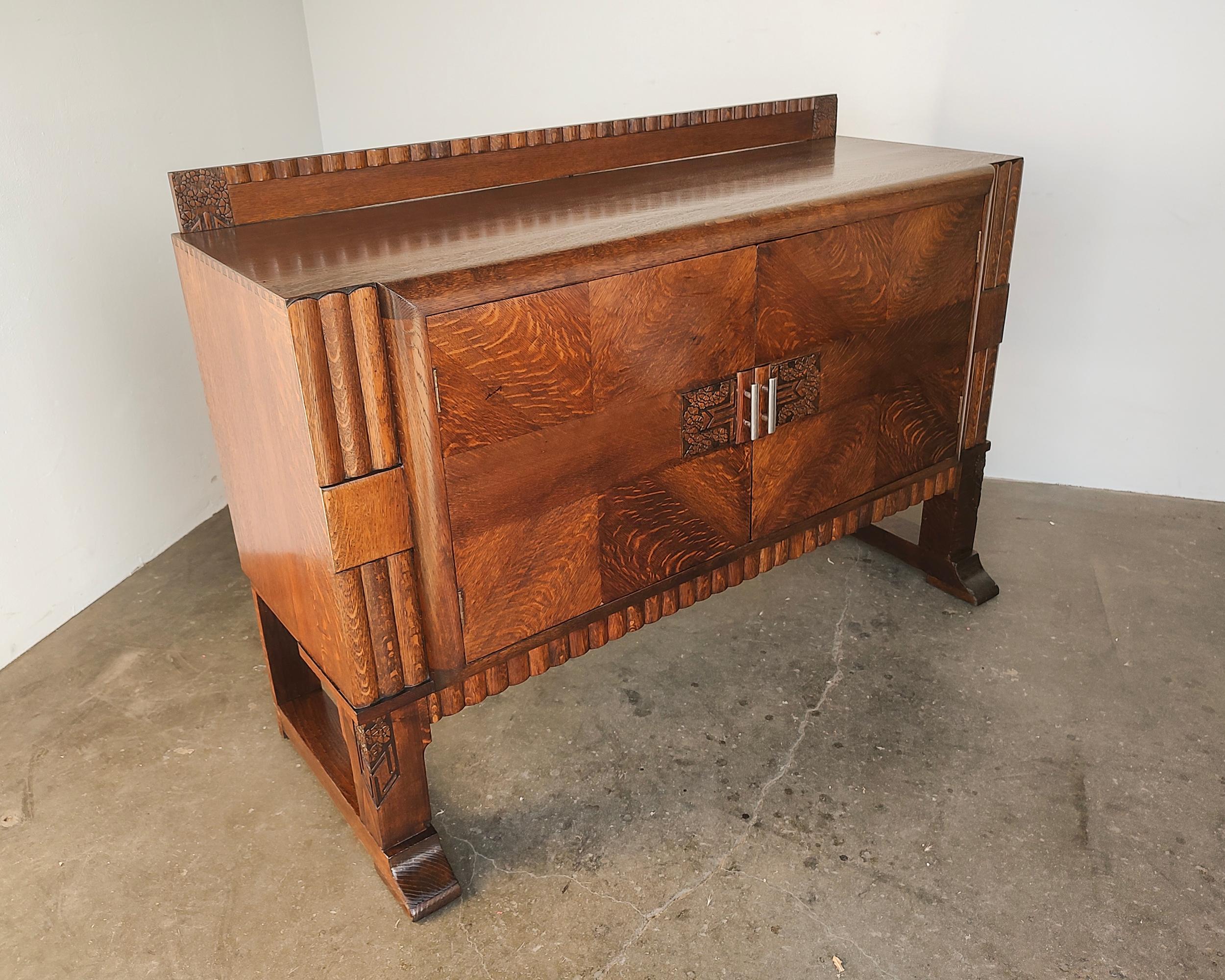 Beautiful Art Deco tiger oak cabinet. Book matched door with hand-carved details, scalloped designs throughout. Cabinet doors open to reveal shelves on each side and four wooden drawers along the middle. Professionally restored. 

57