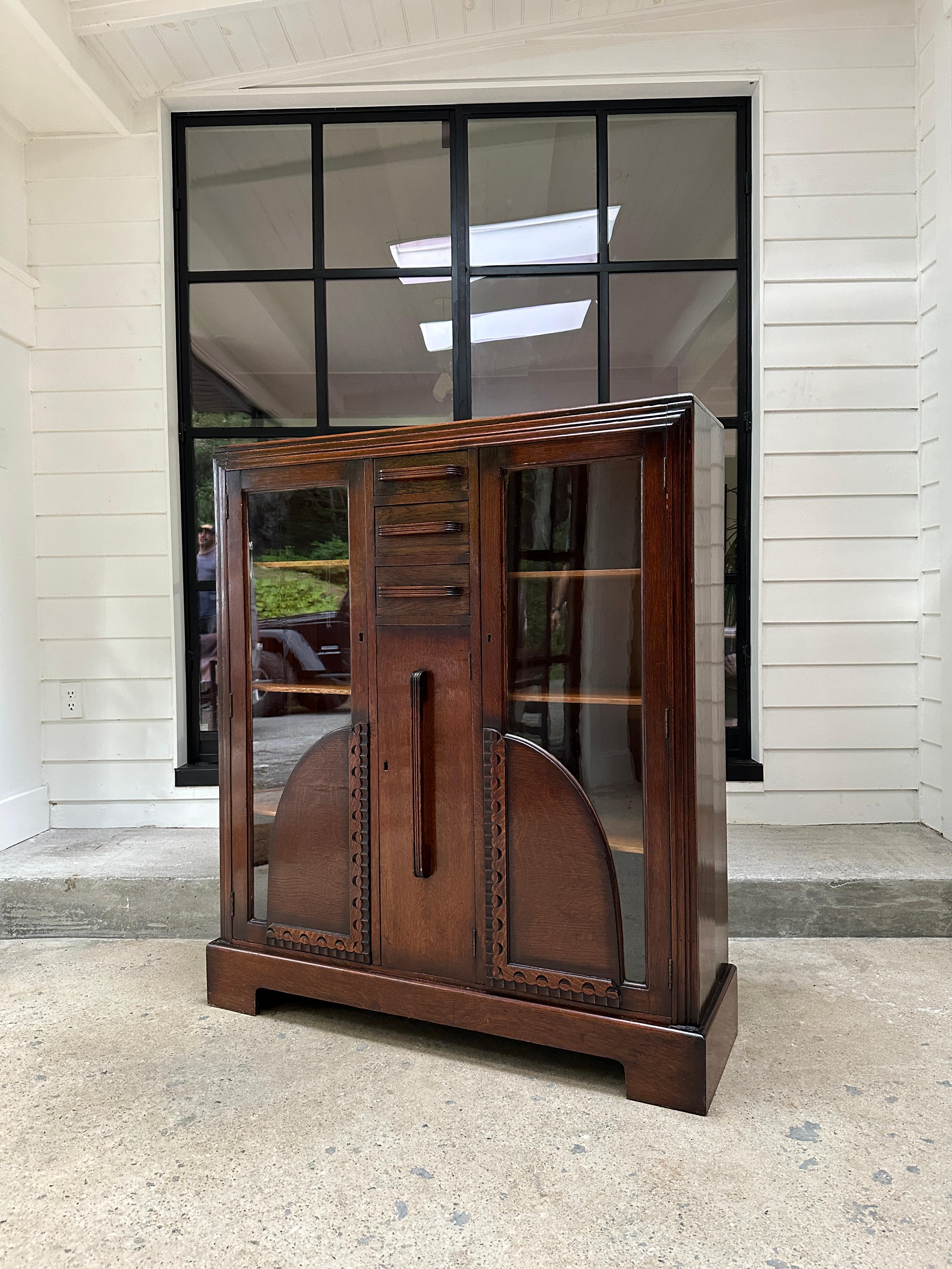 Vintage oak vitrine cabinet featuring two glass doors with three adjustable shelves on each side. Center cabinet holds three small drawers and one medium size storage space with door. This piece represents classic art deco esthetics with its fluted