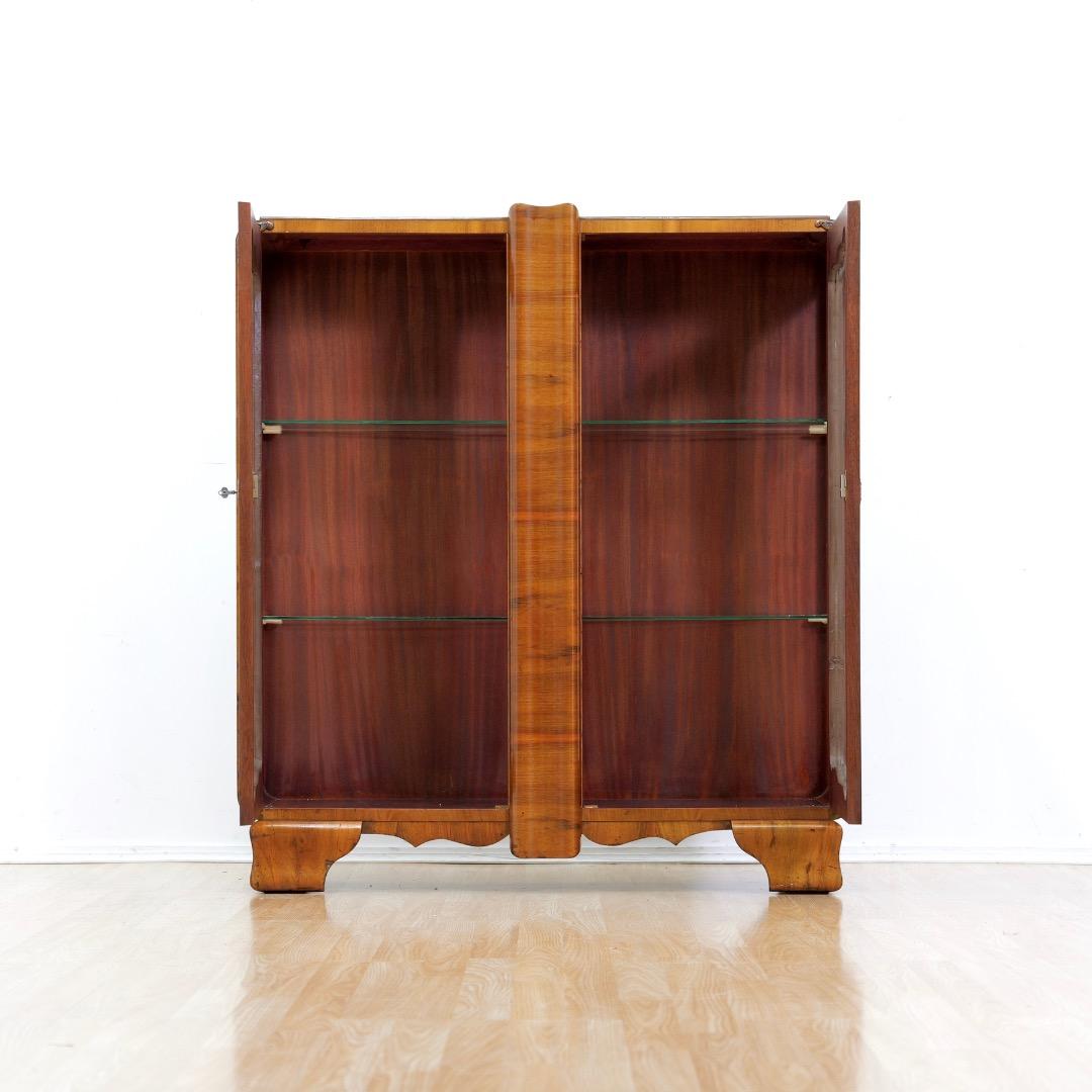Un'elegante vetrinetta Art Deco in noce figurato. Con una forma fantastica, questo meraviglioso mobile ha due ante con decorazioni originali in oro, e all'interno 2 ripiani in vetro ad altezza fissa. Ha le serrature e la chiave originale.