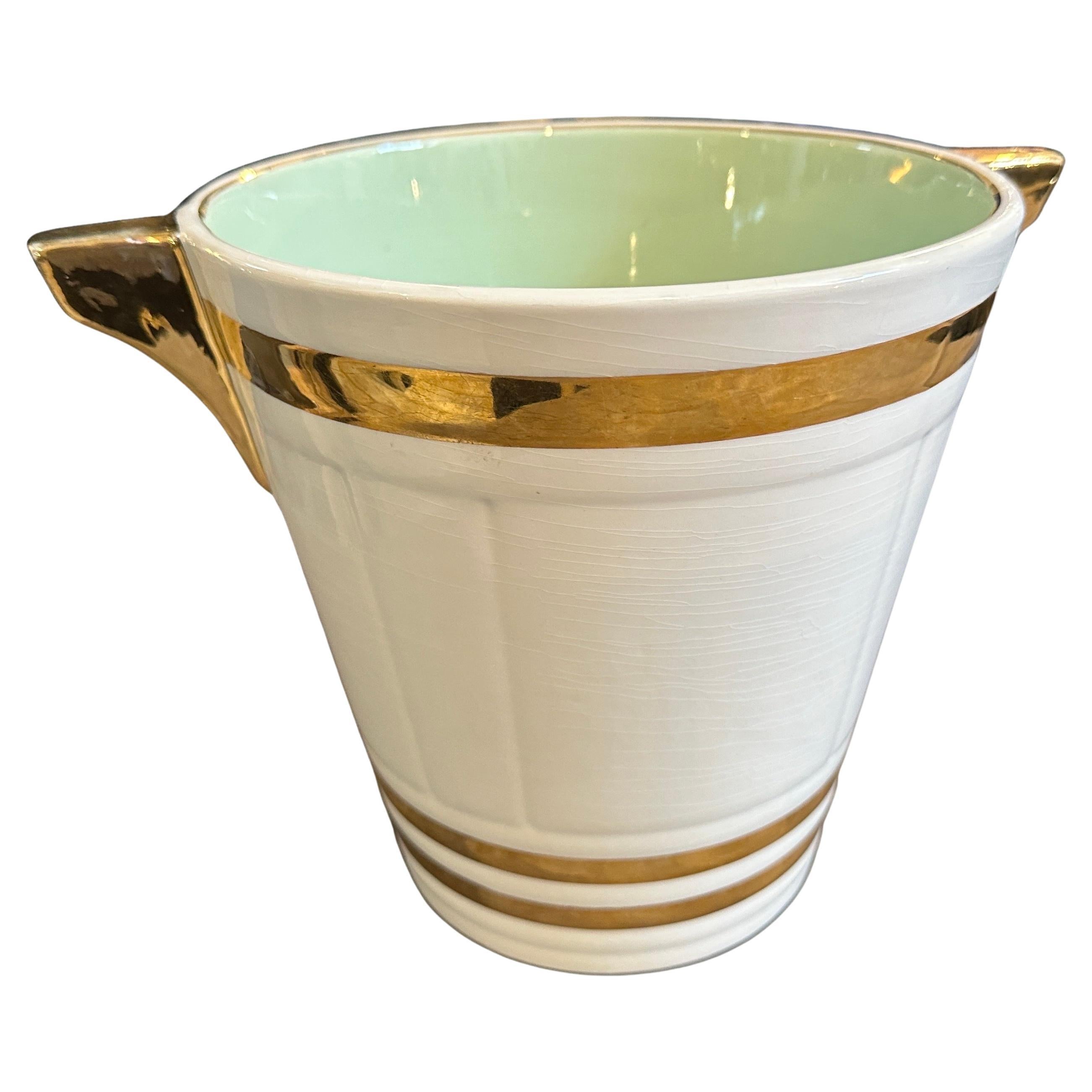 Esta exquisita champañera francesa Art Déco de los años 30, obra de Sarreguemines, es un ejemplo impresionante de elegancia refinada y diseño atemporal. Realizado en cerámica, presenta un rico esmalte blanco acentuado por atrevidas bandas doradas