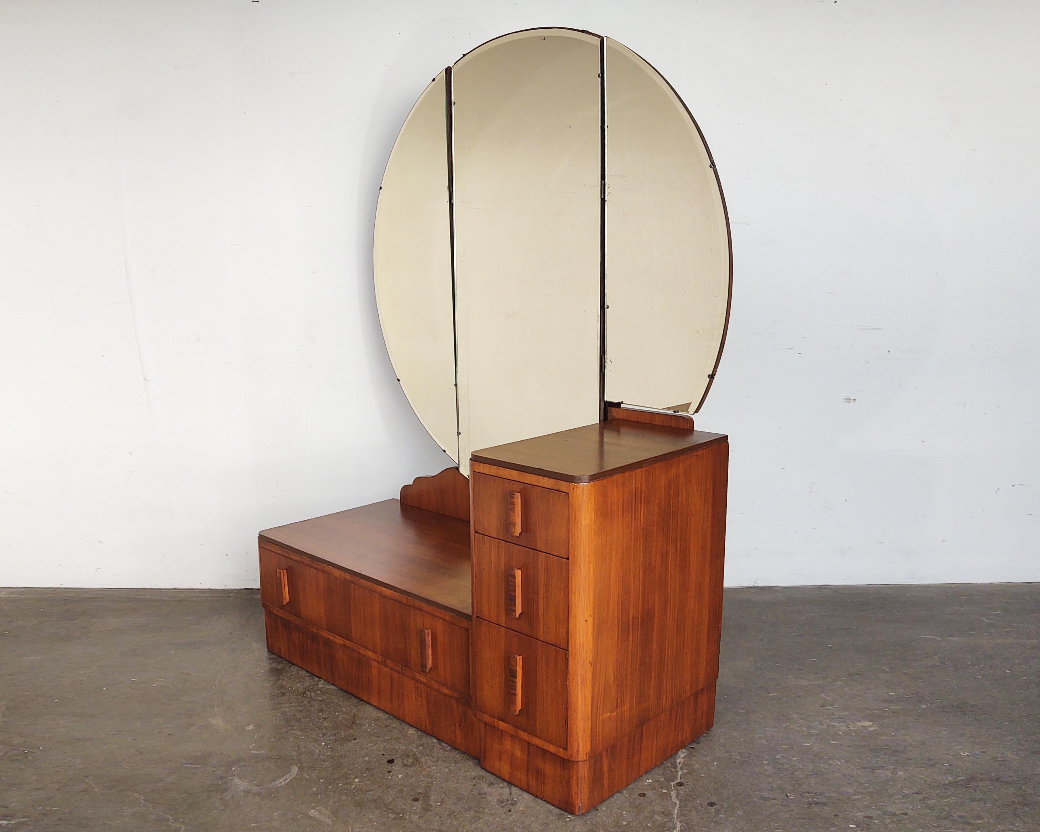Gorgeous Art Deco vanity with walnut base circa 1930s. Four drawers with complementary wood pulls and dovetail joinery. Three-piece round mirror attached to the back with both ends able to pivot forward. Beautiful walnut wood grain covering entire