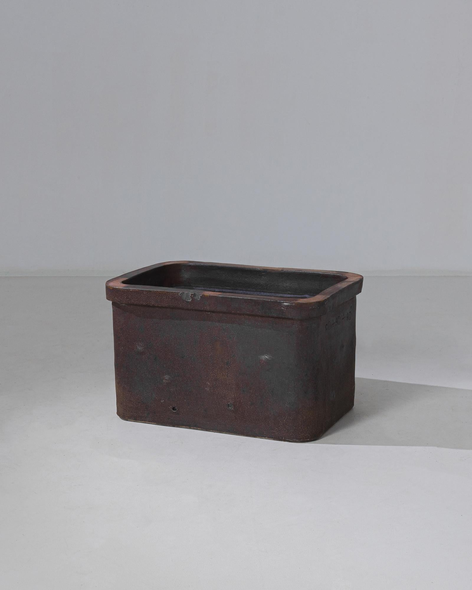 This ceramic planter was made in Belgium, circa 1930. The rectangular form features rounded edges and a thick rim. Seasoned over time, the planter displays a pewter gray patina blended with a reddish-blend hue. A solid and functional display piece,