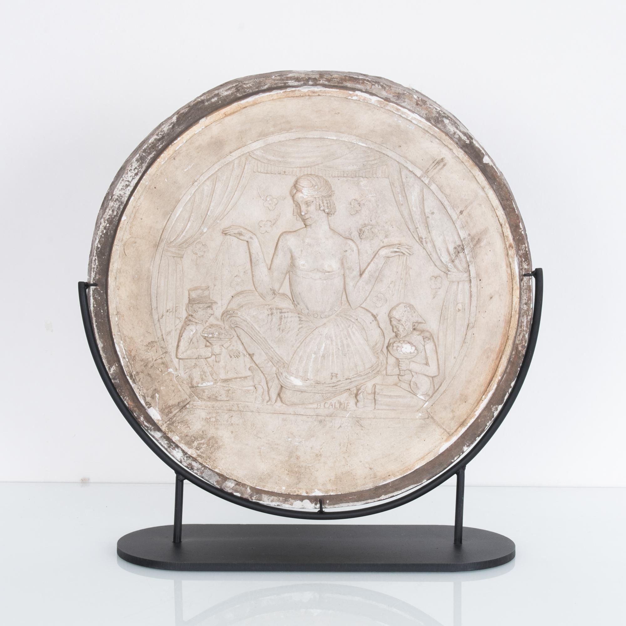 This round plaster decoration was made in Belgium in the 1930s. A white plaster relief, in allegorical art nouveau style, depicts an androgynous, seductive puppeteer being lauded with flowers. A simple metal frame accentuates the fine detail of the
