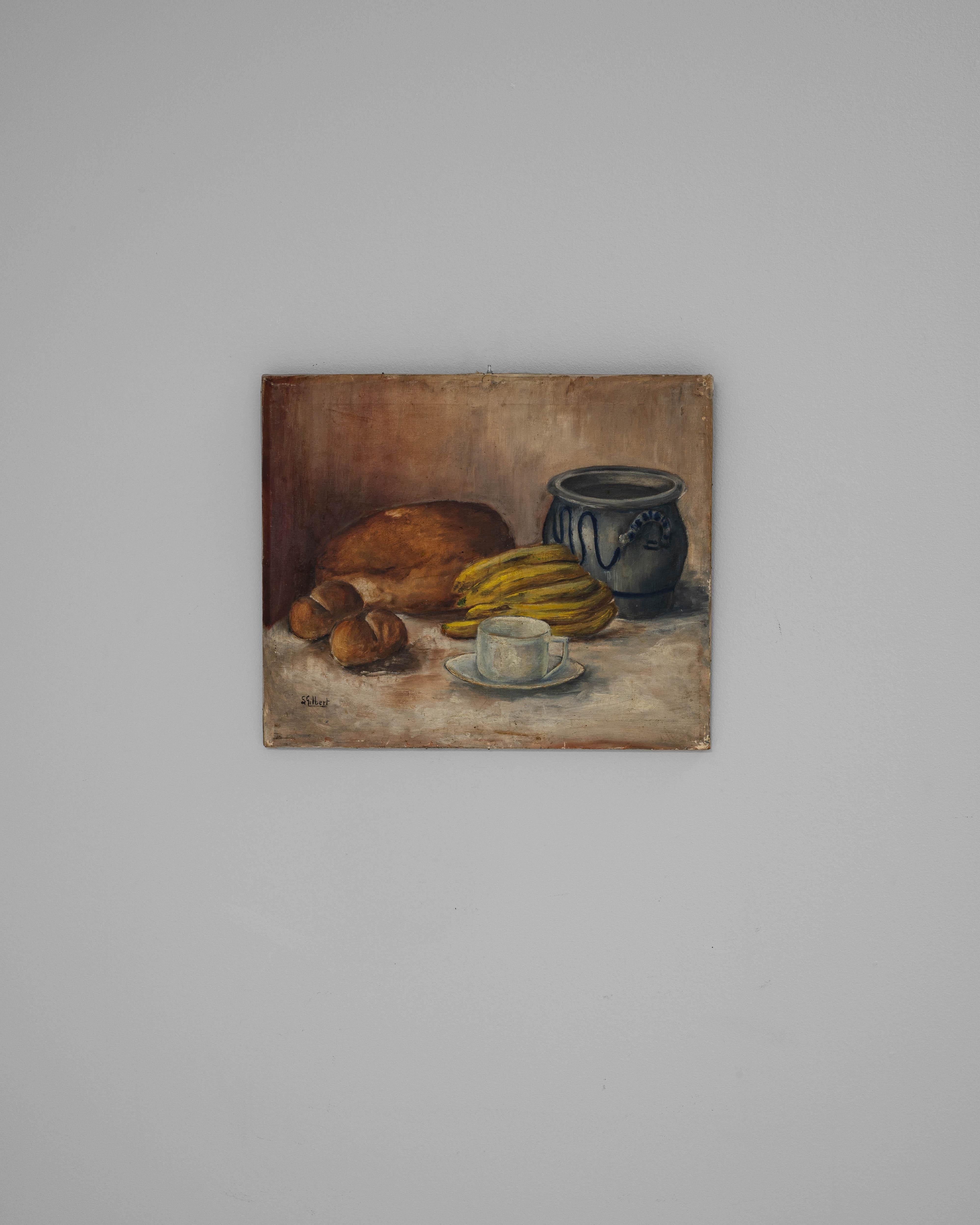 This 1930s Belgian still life painting by S. Gilbert presents a quietly elegant tabletop composition featuring a cluster of baked goods, ripe bananas, a rustic ceramic vessel, and a solitary cup and saucer. Executed in oil on canvas, the work