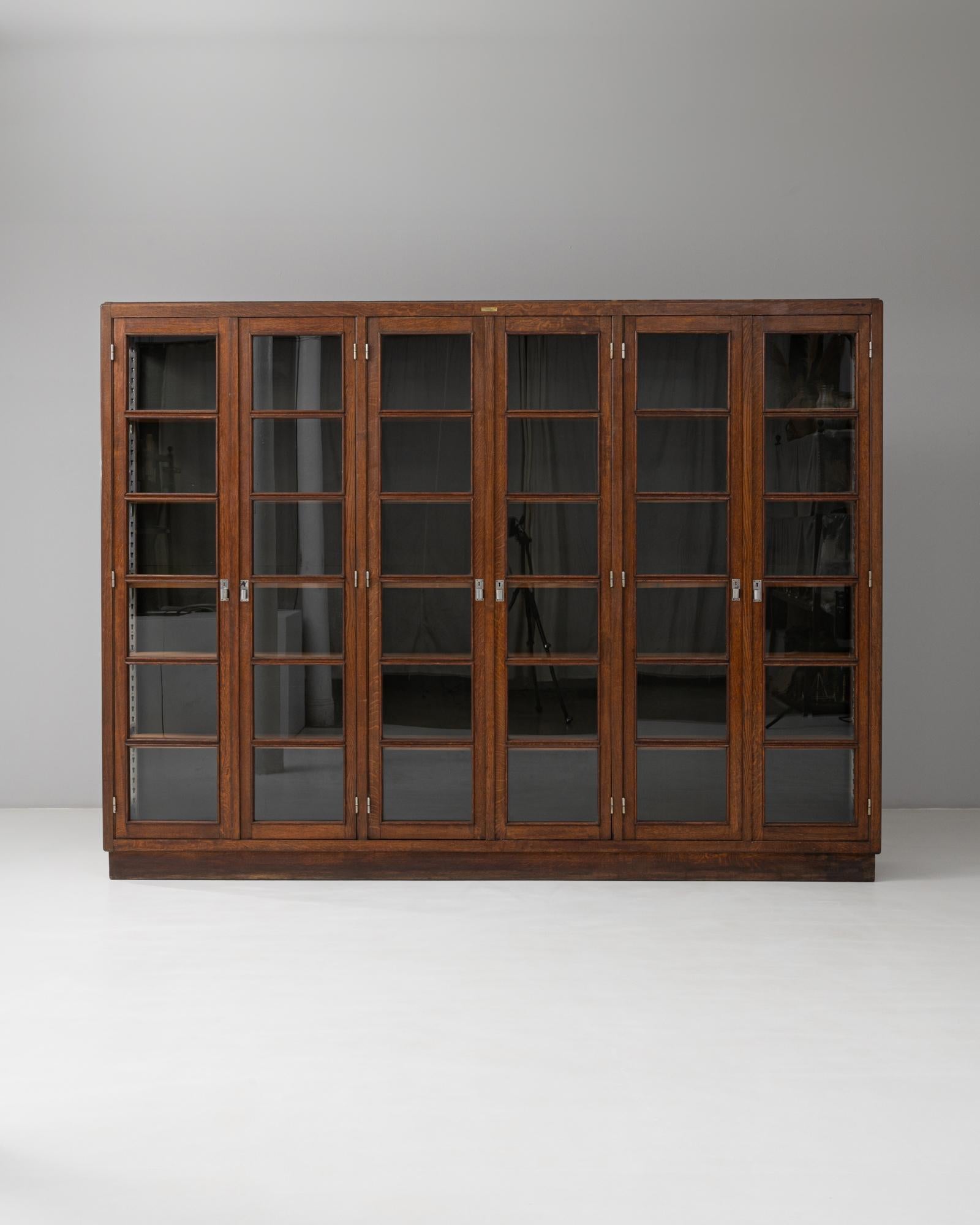 This 1930s Belgian wooden library display case is a striking example of functional design combined with timeless craftsmanship. Featuring eight framed glass doors, it offers expansive storage and display space across multiple adjustable shelves,