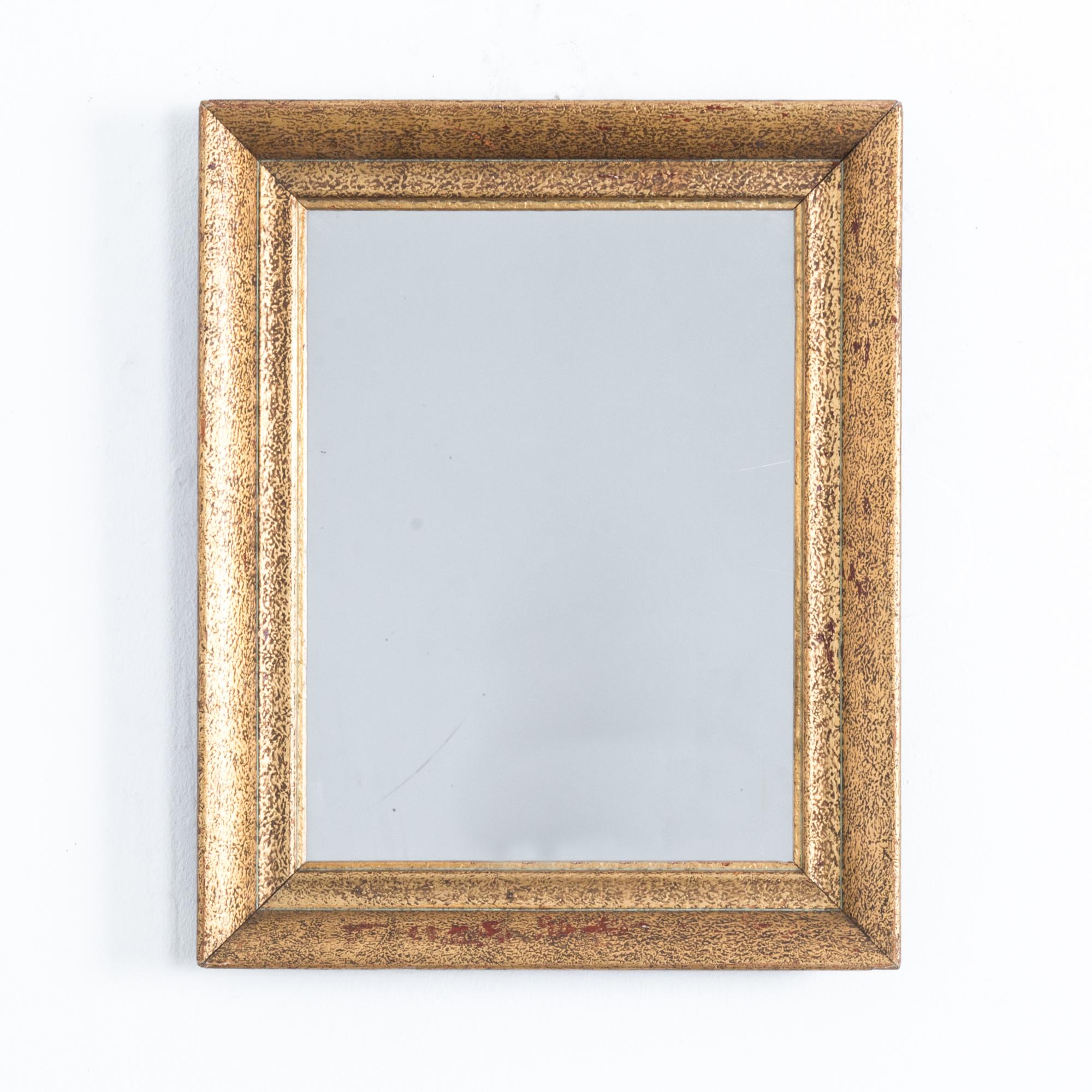 A mirror with a rectangular gilded frame from Belgium, circa 1930. A textured finish creates a patinated effect, revealing a coppery undercoat beneath the gold. The wide angles of the frame add depth to the reflection. Simple lines are enhanced by