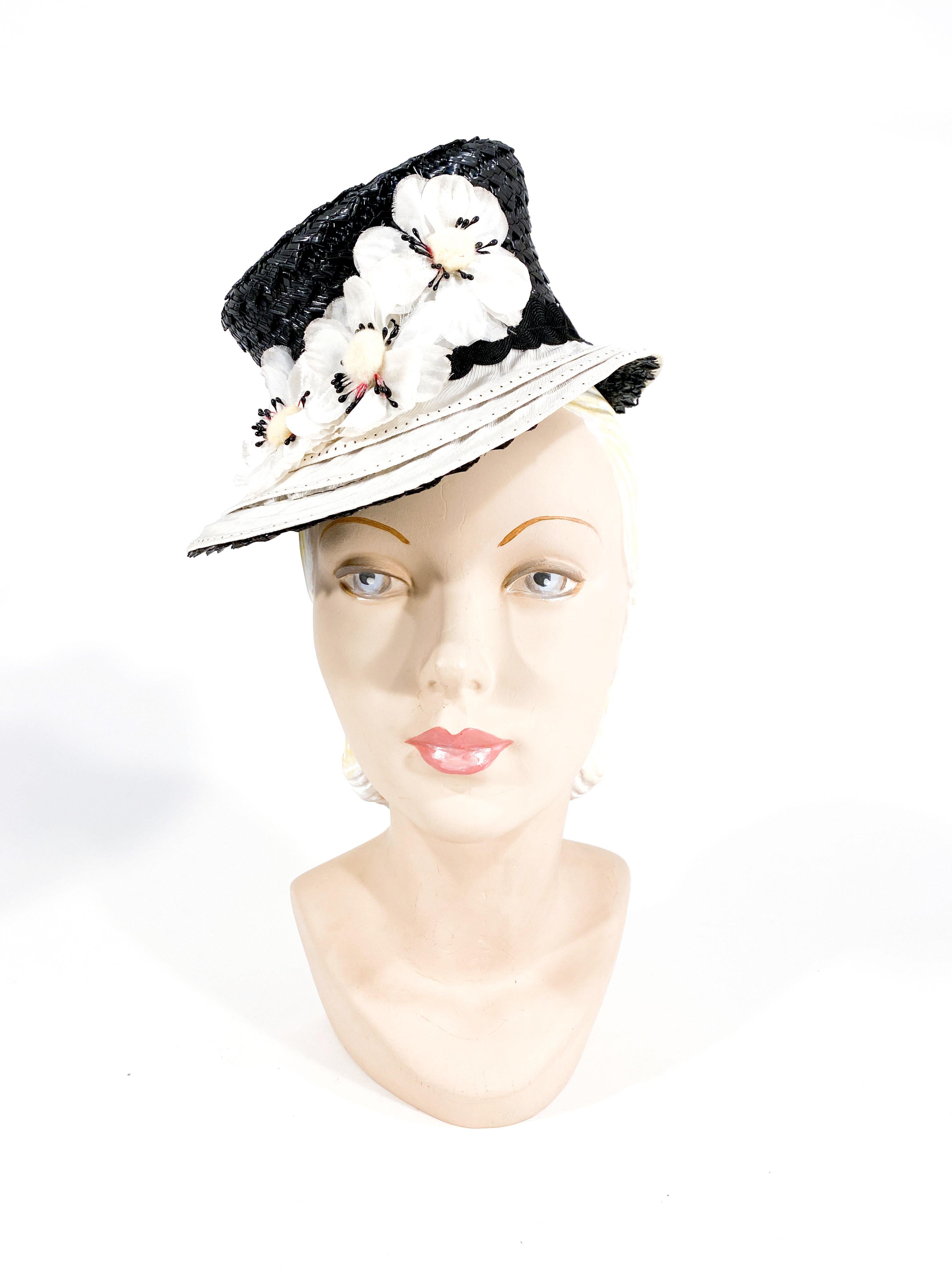 1930s Art Deco black coated woven straw hat with 3 layers of off-white twill rows on the brim accented with black top stitching. The band of this hat has two intertwined bric-brac trimmings accented with white velvet and silk flowers. The interior