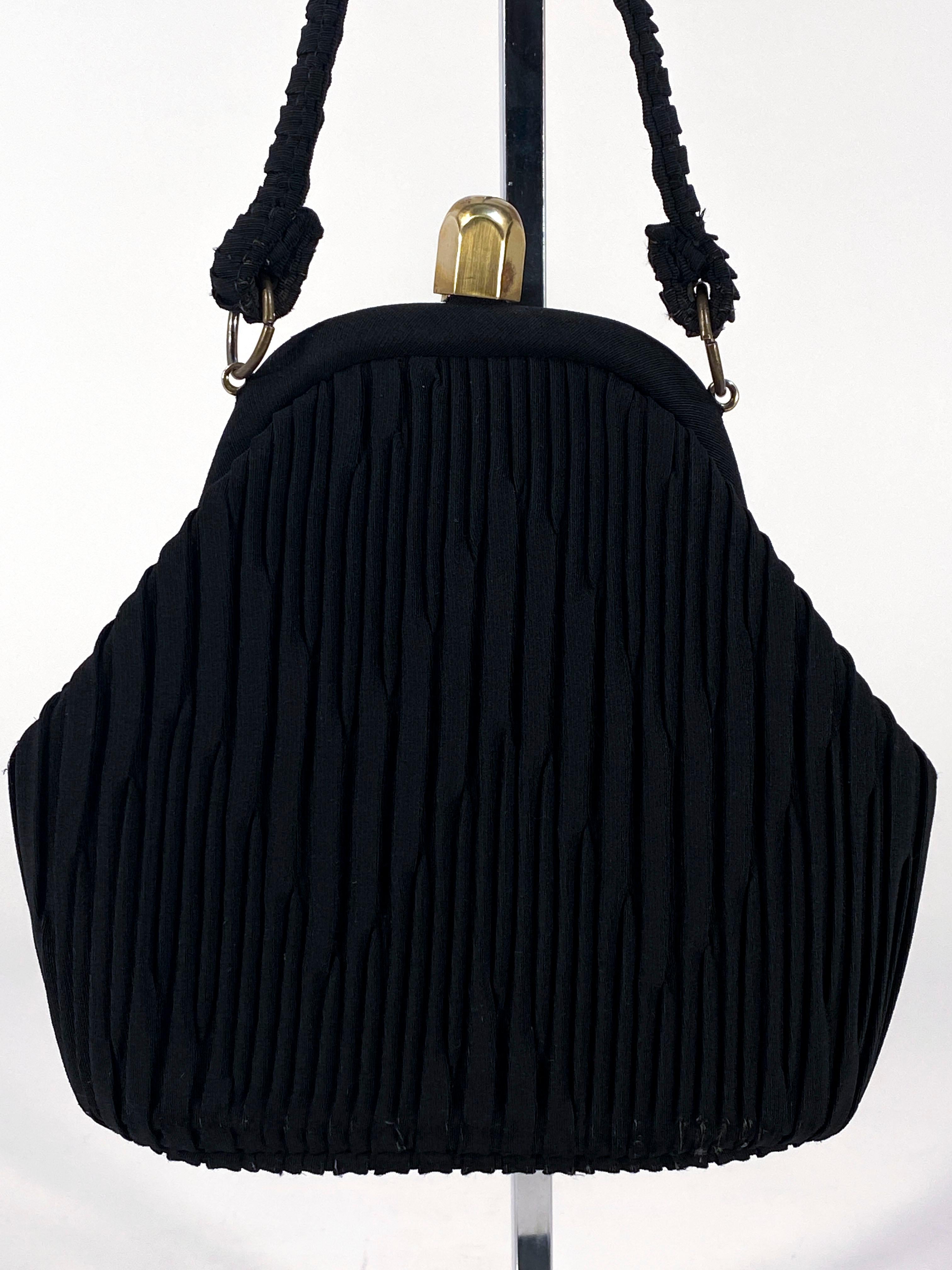1930s Black Art Deco hand back with intricate decorative knife pleating in a zig-zag pattern on both sides of the bag. The handle has matching pleats and the inside frame/closure is made of brass. The interior is lined in a soft pink with a built in