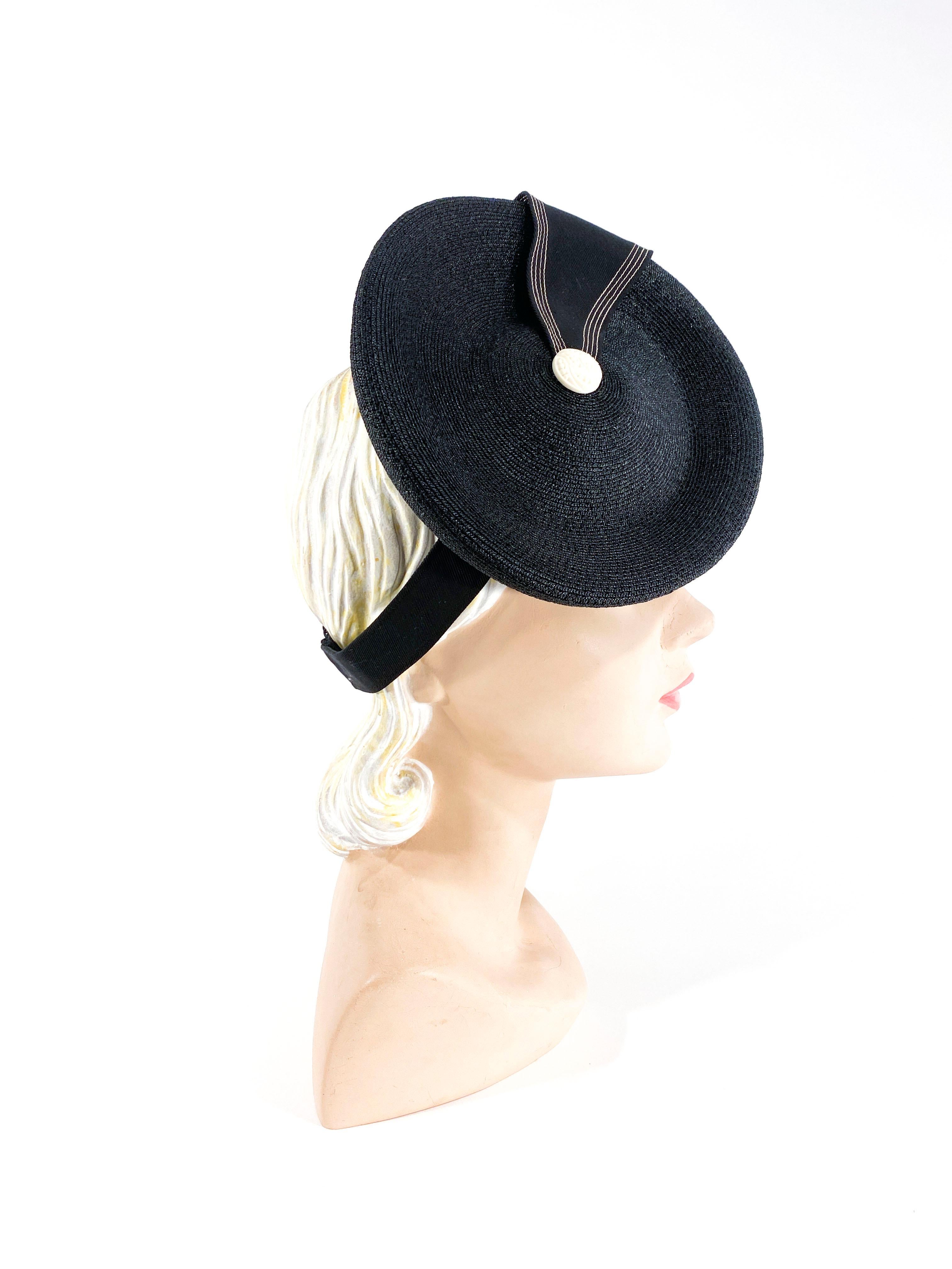 1930s black perch hat made of a coated woven straw decorated with a Nautical-esque smart twill embellishment with off-white top stitching, and decorative period buttons. The back has the wide gathered security strap to affix the hat to the head. 