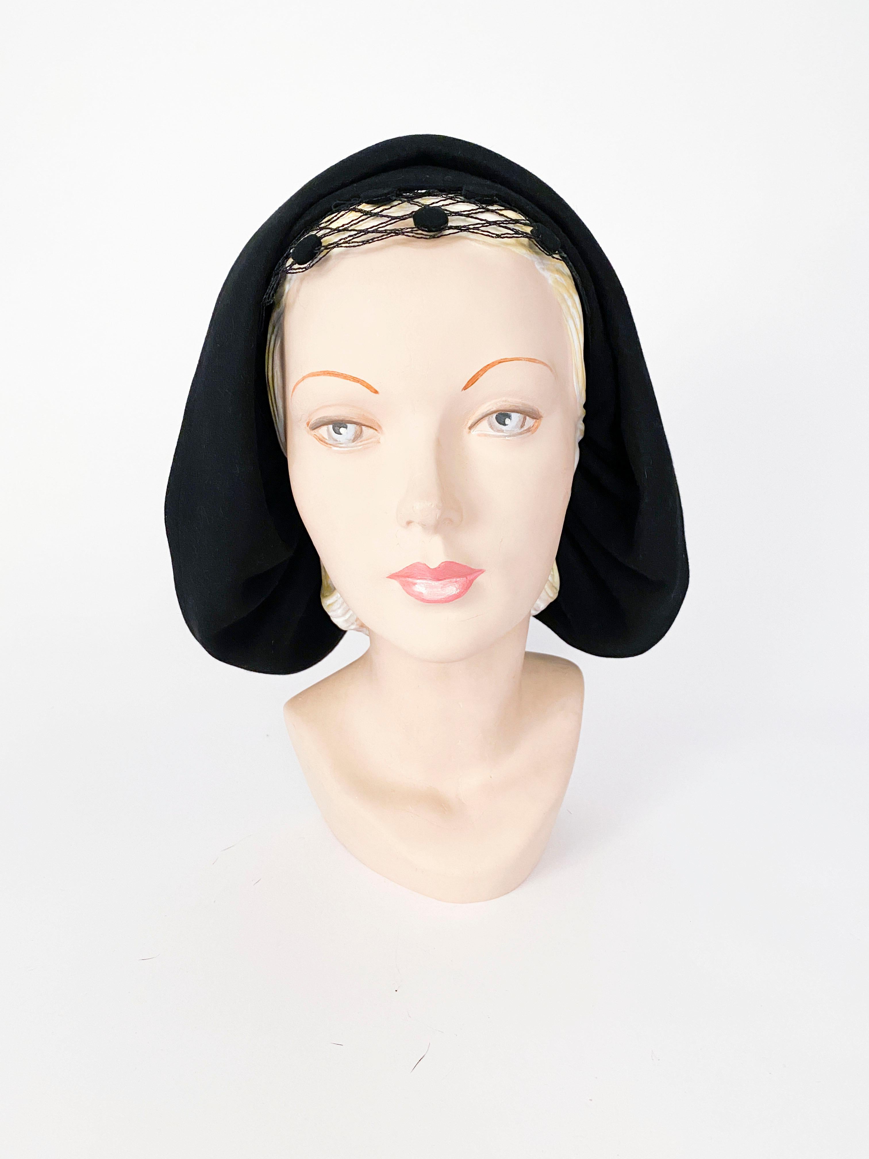 1930s black fur felt hat that is ruched along two black panels. The back cut-out panel is adorned with a double layer of netting and the front has a short net accented with felt circles.