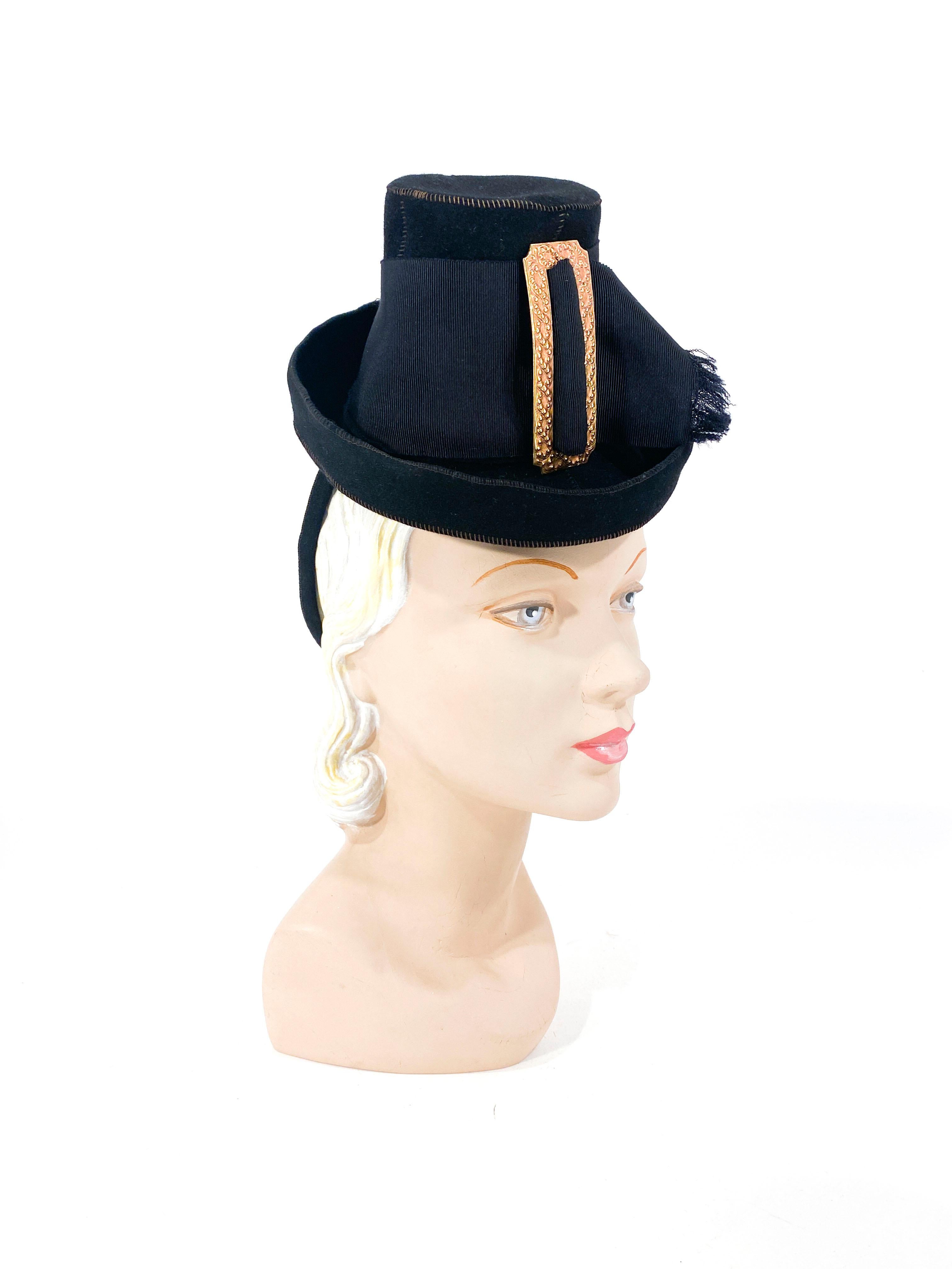 Sombrero de peregrino de juguete de fieltro de piel negro de finales de los años 30, con una ancha banda de cinta de grosgrain y una gran hebilla decorativa de latón. La anilla de seguridad estructurada está recubierta de fieltro de pelo negro a
