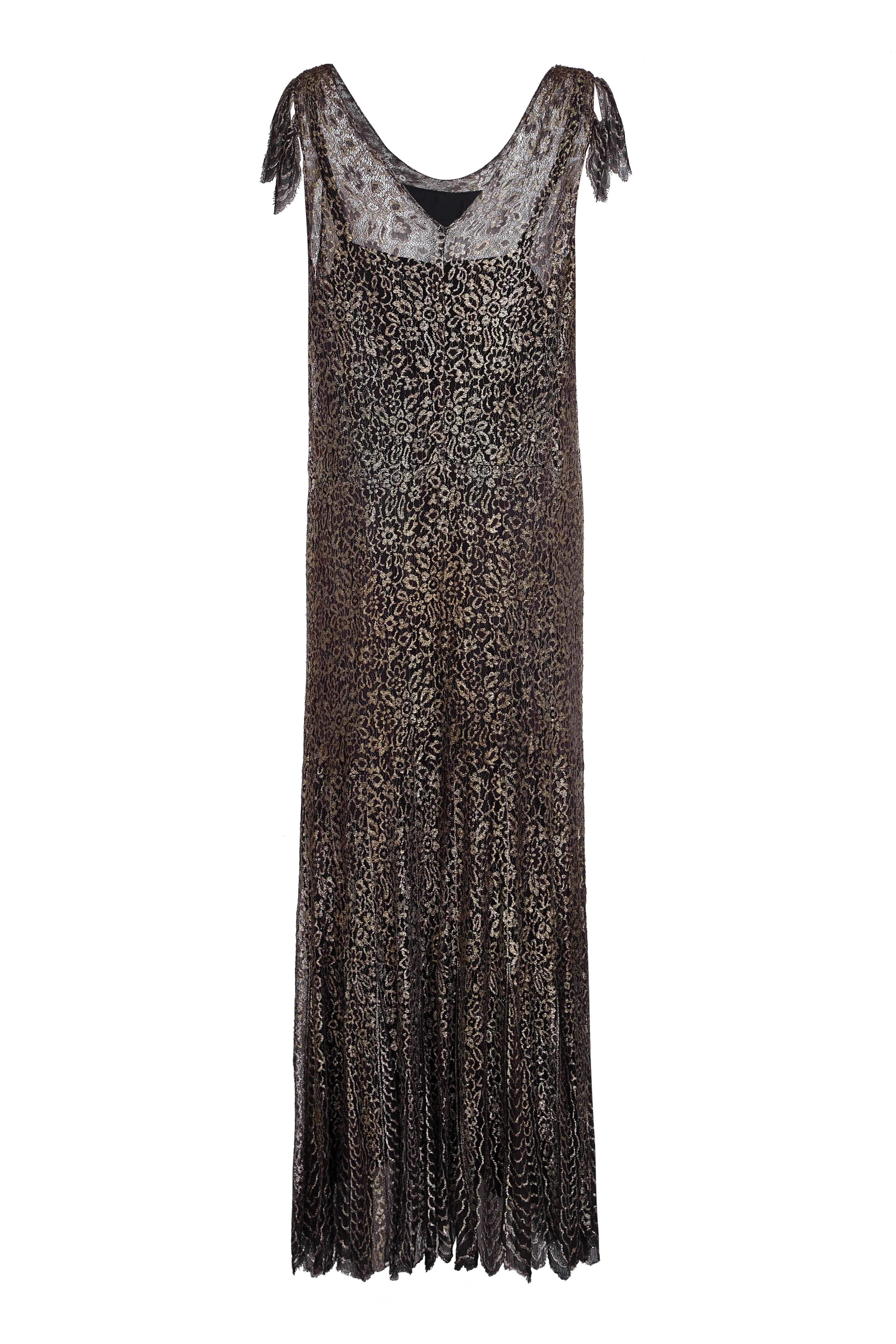 Este slip dress de finales de los años veinte o principios de los treinta destila glamour. El encaje negro y dorado tejido se conoce como encaje de telaraña y es muy apreciado de esta época. El vestido sigue una línea alargada, que fluye sobre el