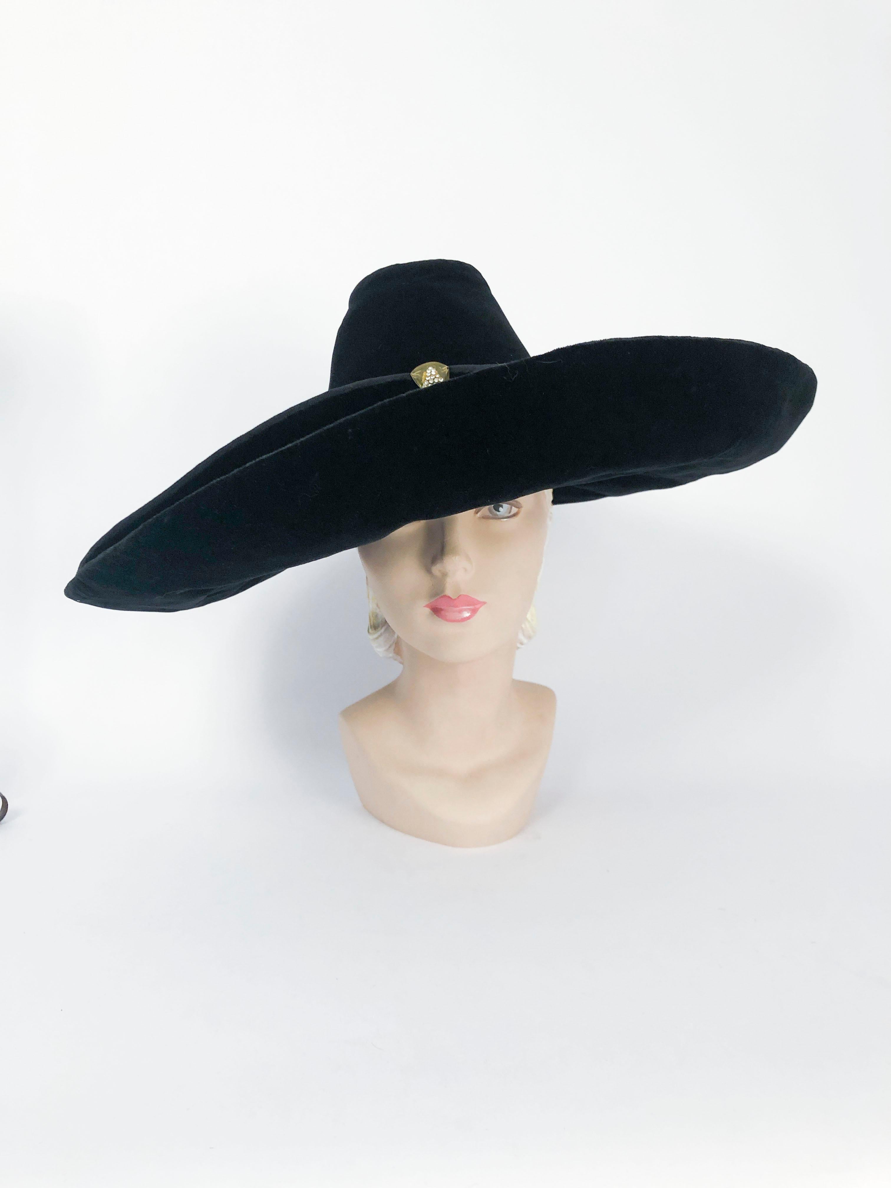 chapeau noir des années 1930 en velours et sergé avec accent en bakélite et strass. Couronne haute et large bord roulé. Ce chapeau faisait partie des années dorées d'Hollywood et fait référence au glamour de l'époque