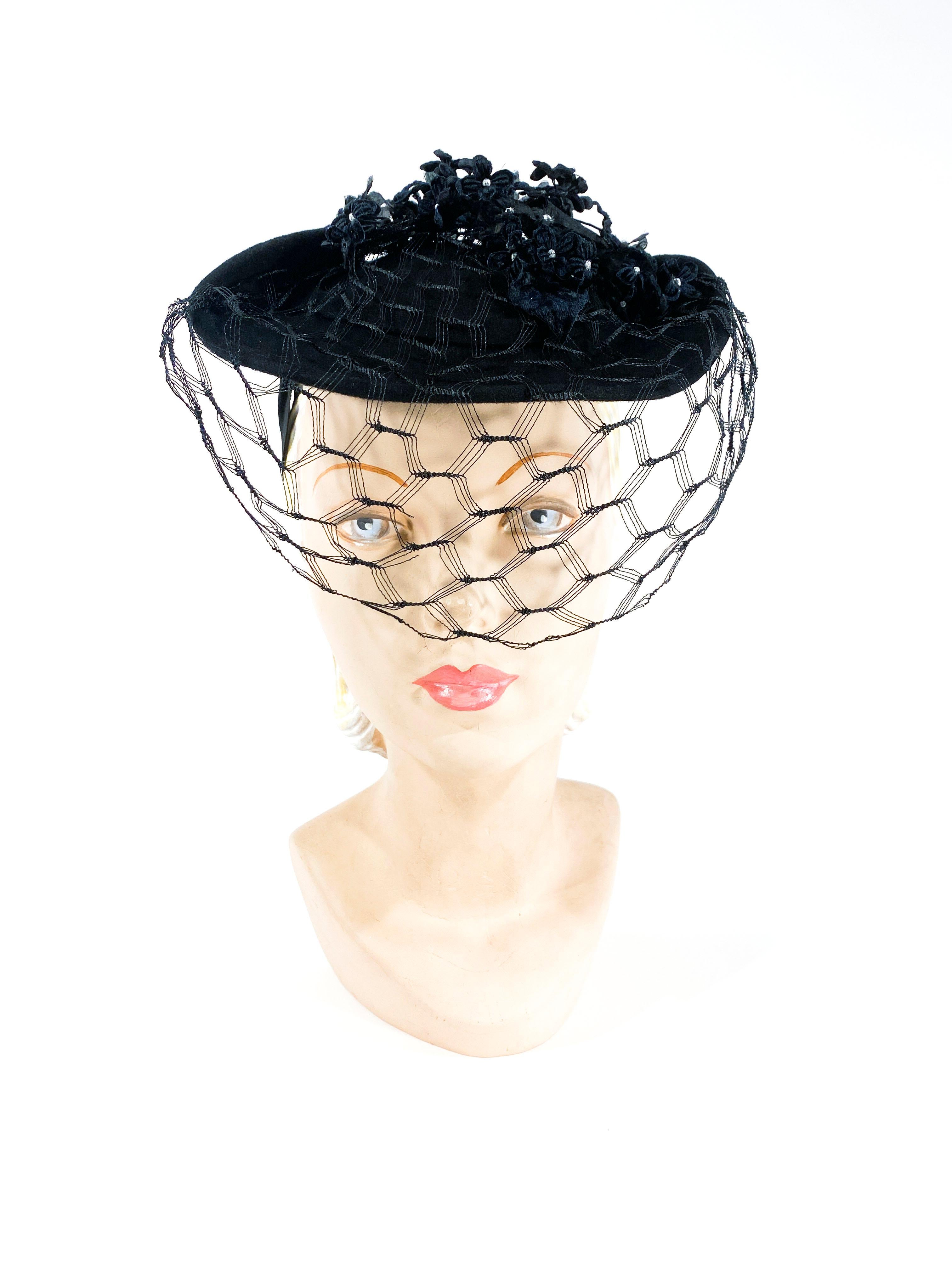 1930s black fur felt handmade hat decorated with textured satin and velvet flowers and leaves. The front of the hat has a half-faced veil and the back has a gros-grain security band to fix the hat to the head.