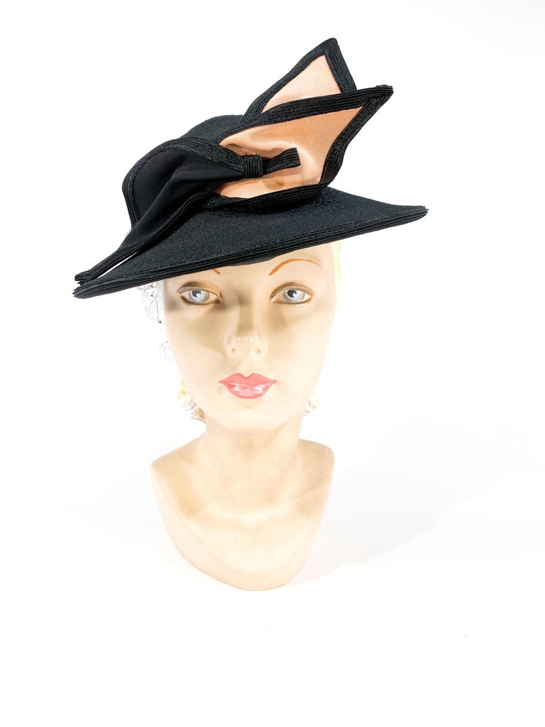 1930s black daytime coated raffia hat with an Art Deco Bow in black and peach twill. The grosgrain hat band is finished with an enlarged back net accent with peach velvet polkadots. Note this is a perch hat meaning it is meant to be worn cocked to