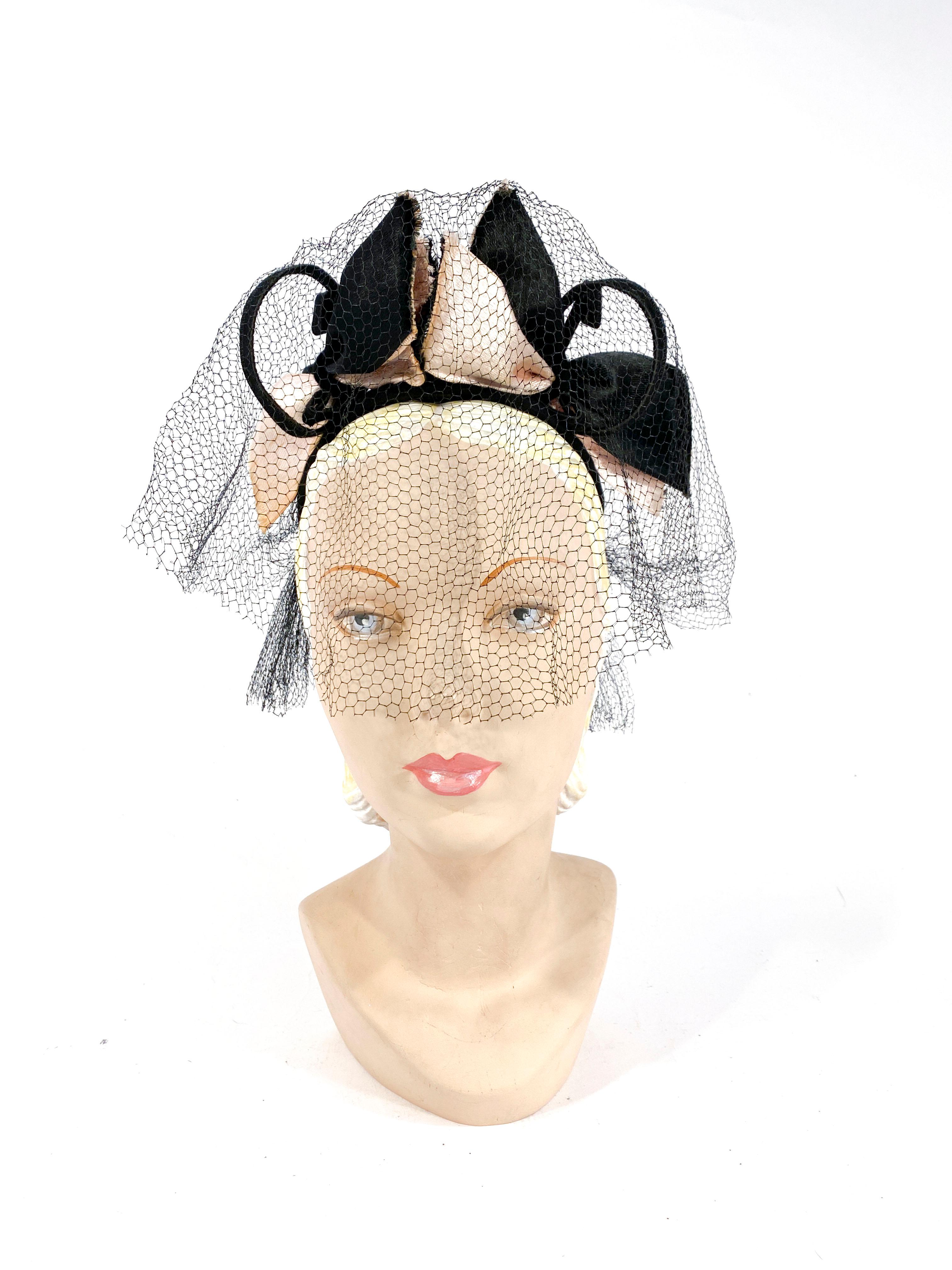 1930s black sculpted hat with light pink and black satin bows adorned with wired hoops. The veil covers the eyes and nose. 