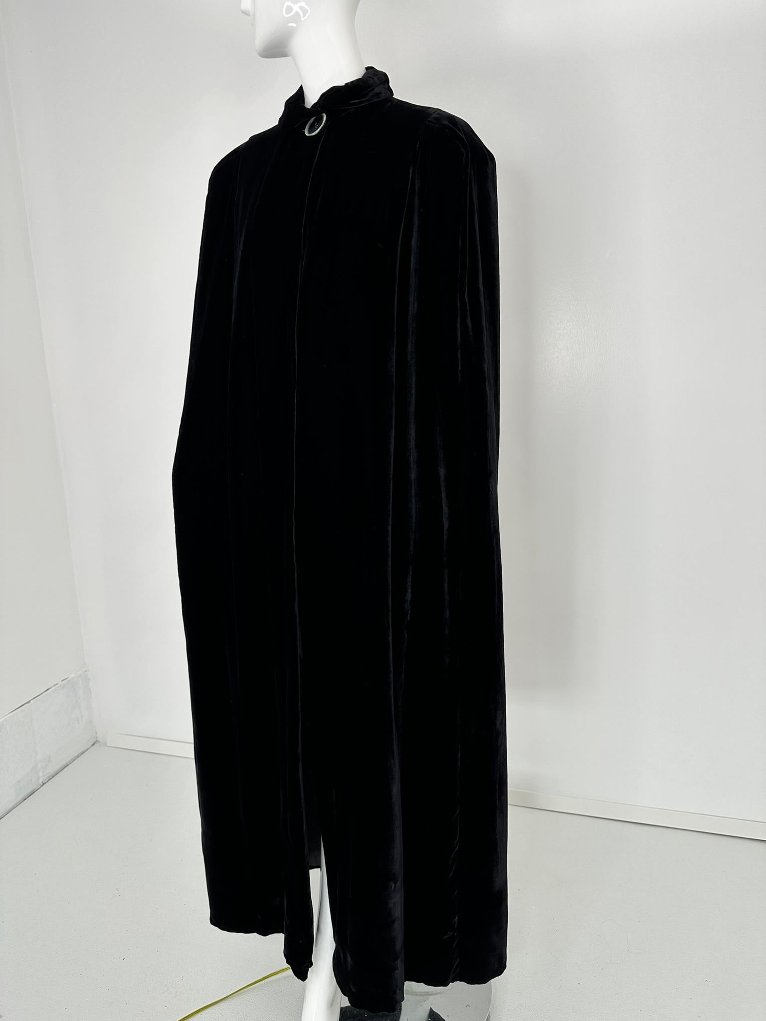 Mantella da sera in velluto nero degli anni '30 con colletto a balze e un grande bottone bianco e nero sul collo.
Drammatica mantella a tutta lunghezza in velluto nero setoso, la mantella si drappeggia sulle spalle e cade in una linea ad A fino
