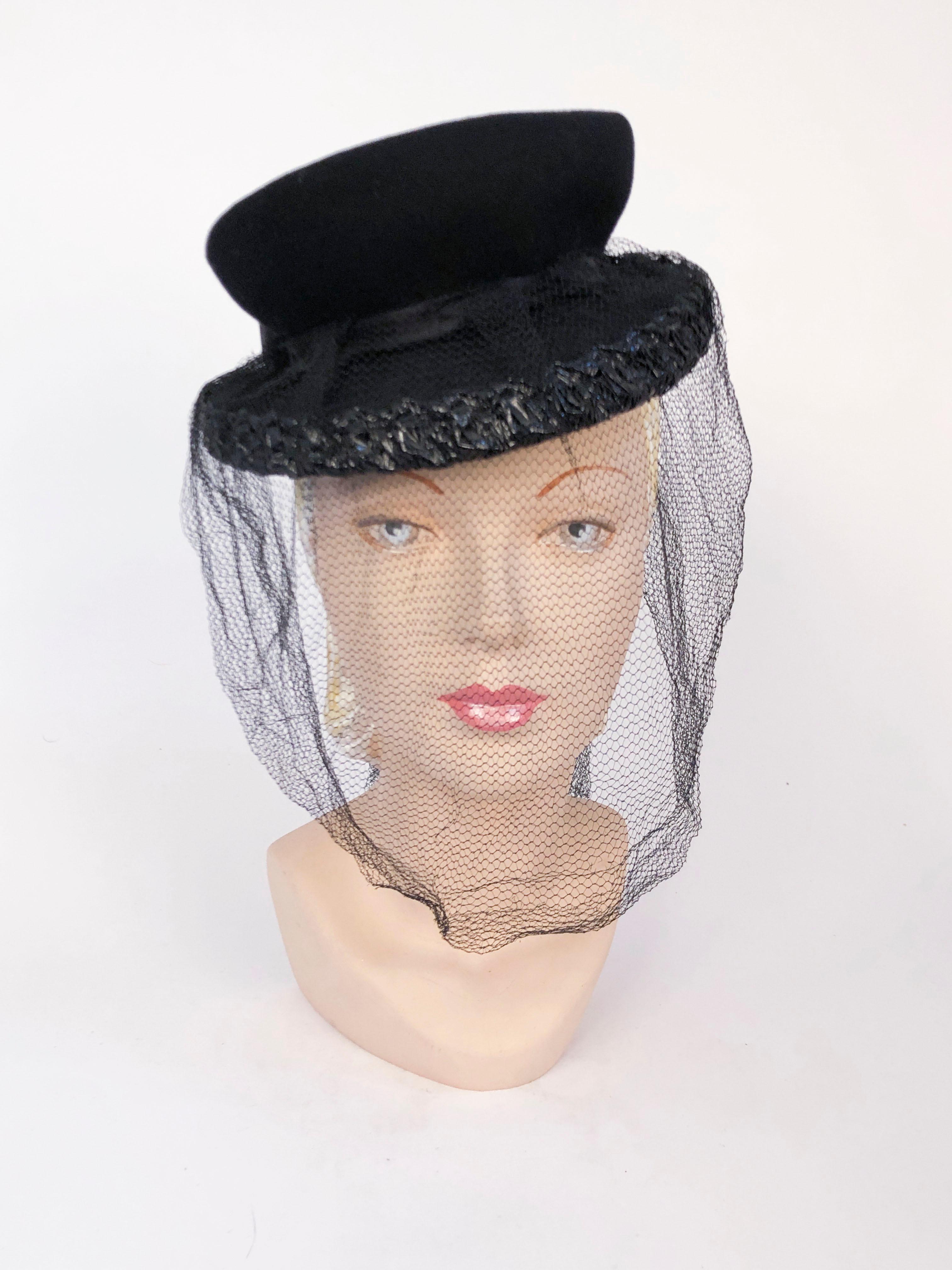 Late 1930's, early 1940s Black hand-sculpted wool perch hat trimmed in black shiny raffia and features a black silk satin band and oversized bow on the back. The veil is full-face coverage and has two tails that accent the satin bow.