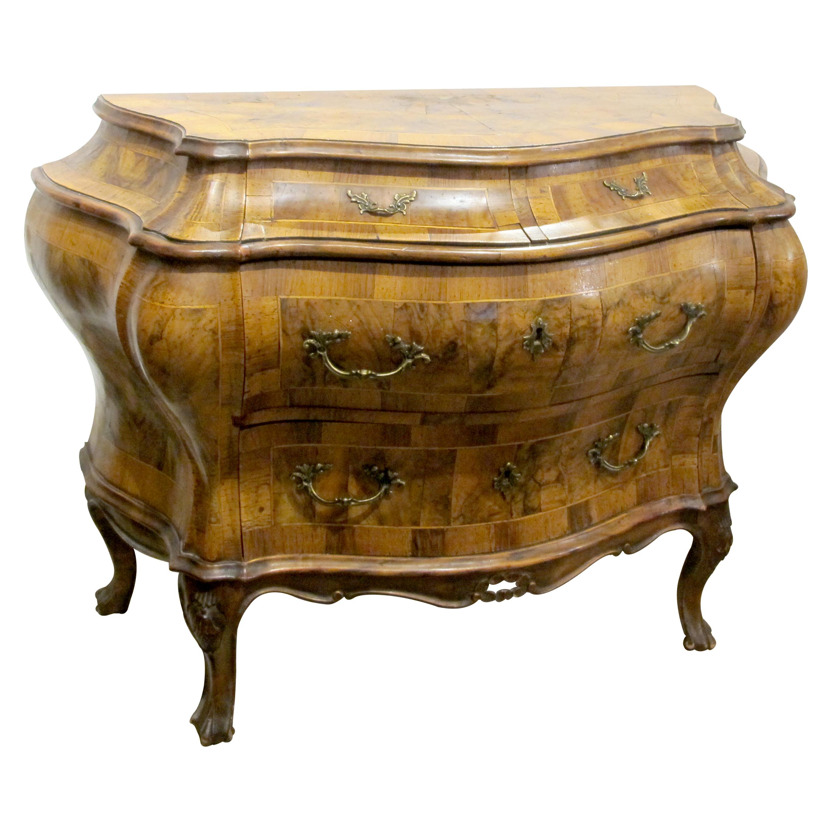 This Italian 1930s bow-fronted chest of drawers is masterfully crafted with intricate olive wood and walnut marquetry. The piece is designed in the Rococo style, characterised by its elegant curves and fluid forms. The chest features two large