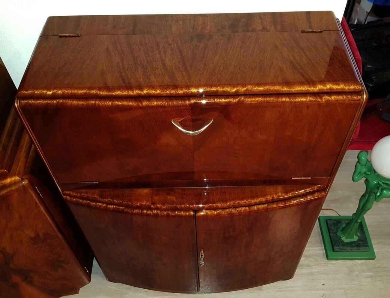 This vintage Art Deco cabinet features a bowfront design that provides a gently curving contour that is visually and stylistically pleasing. Made of a bookmatched burl walnut on the cabinet's exterior with the interior veneered in a ribbon figured