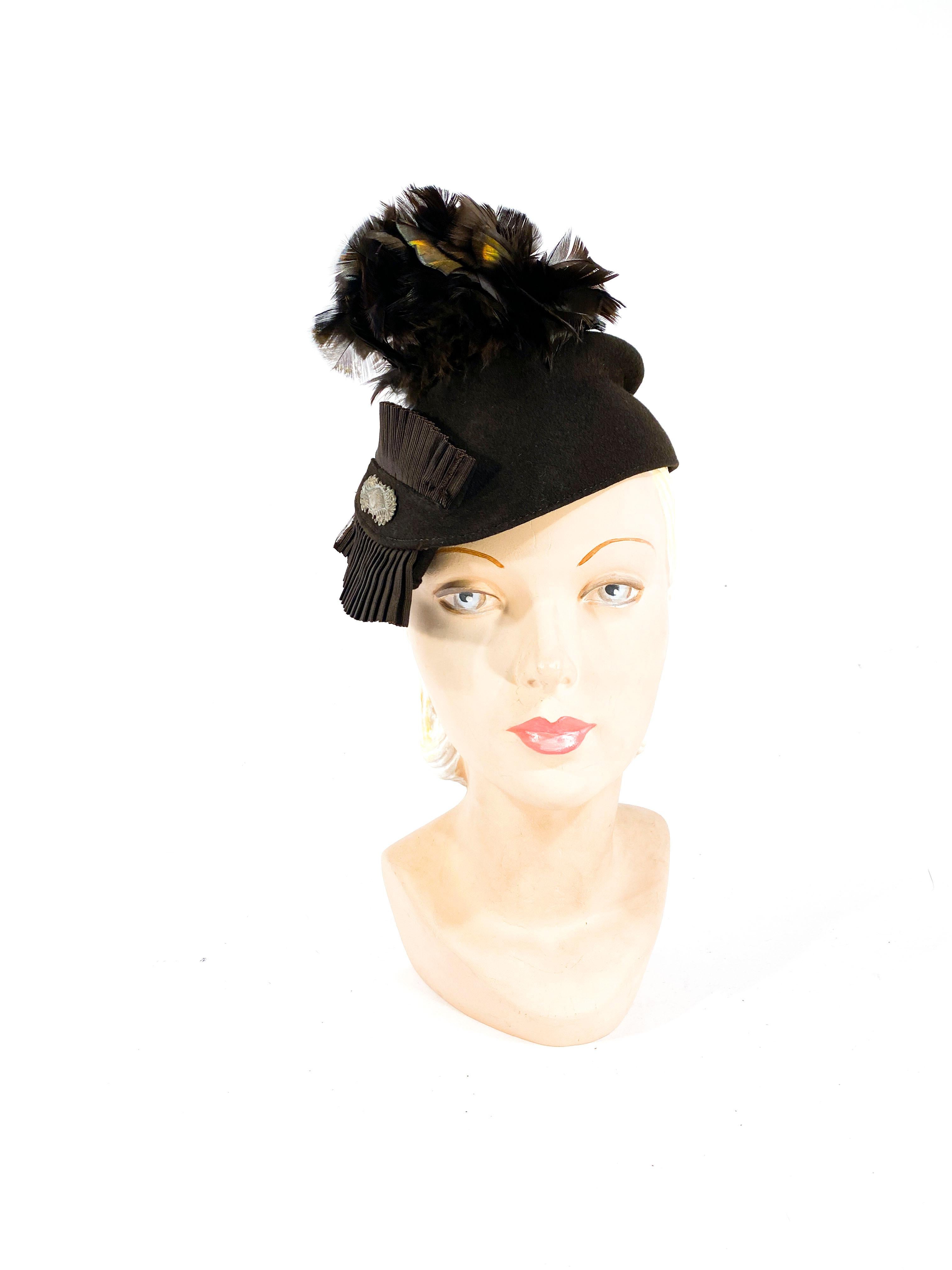1930s Brown Sculpted beaver fur felt hat with an asymmetrical silhouette. Decorated with feather flowers, and a pleated grow-grain ribbon centered with an elongated brass art deco accent. 