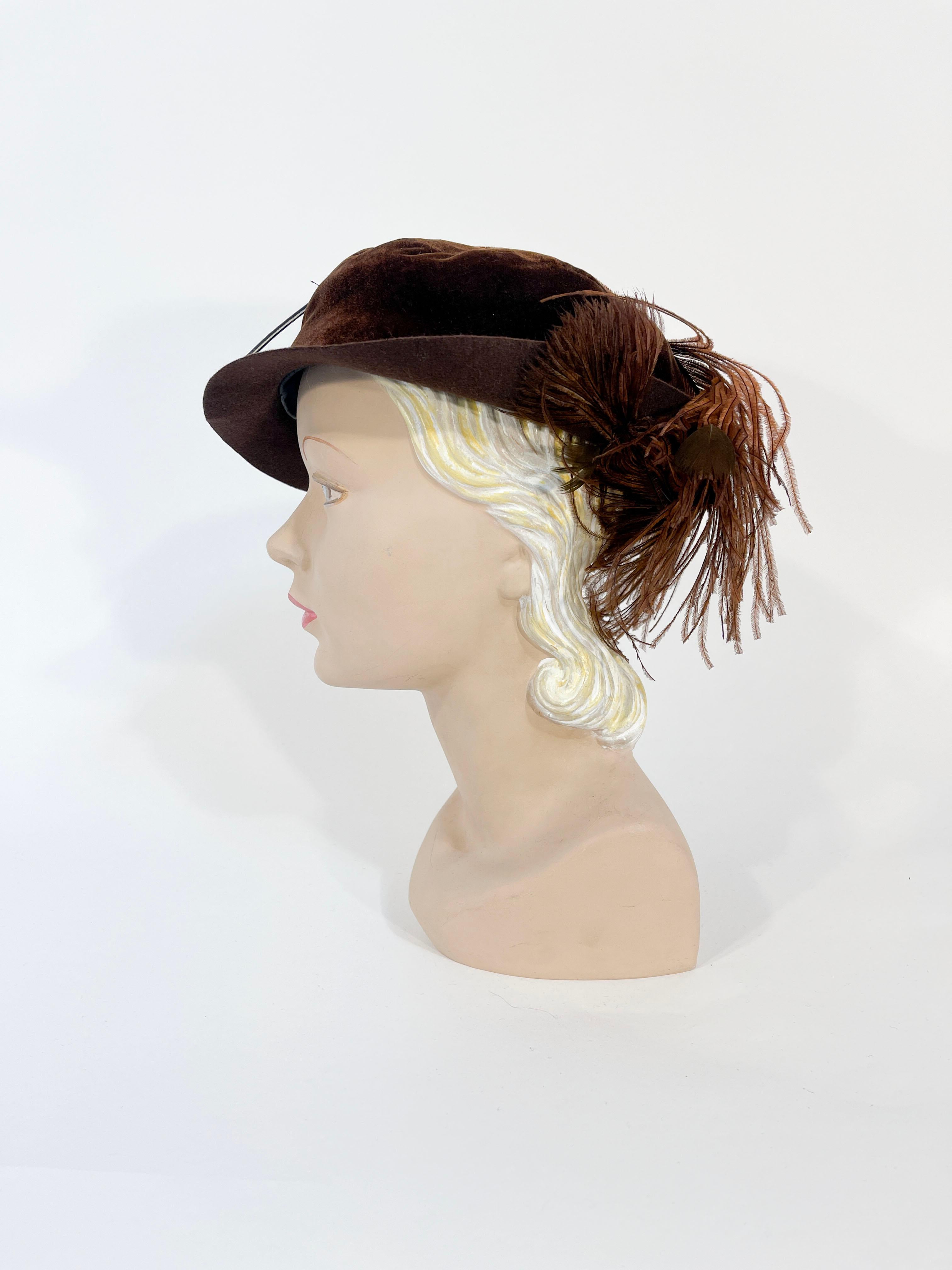 Early 1930s brown wool felt hat with silk velvet covered crown, a hand shaped narrow brim, and an enlarged hand dyed brown ostrich feather sewn down into a stylistic motif where the feather curls beneath the brim. 

The interior is lined in a black