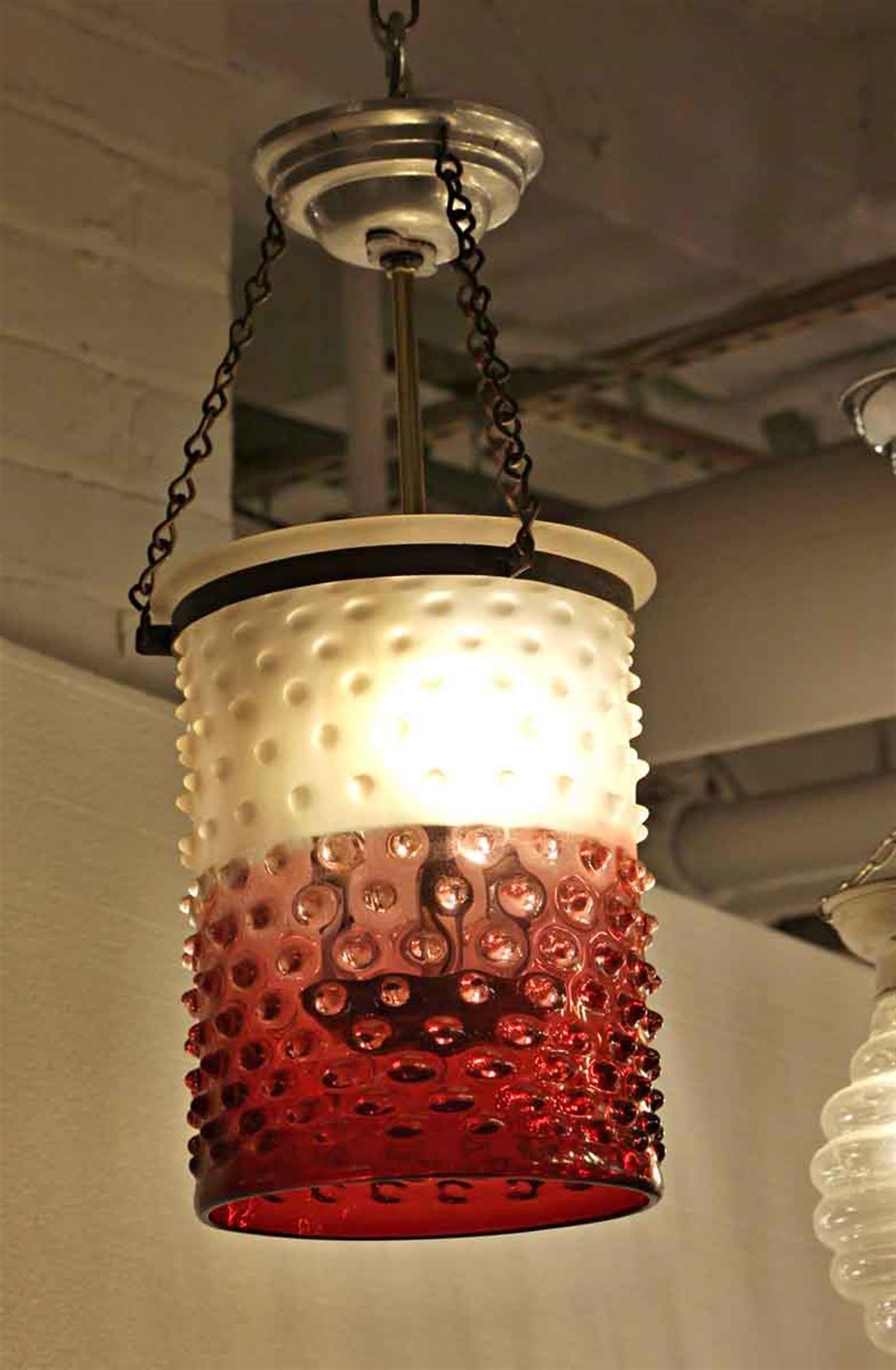 1930s cranberry and white colored glass textured pendant light with a brass frame. This can be seen at our 2420 Broadway location on the upper west side in Manhattan.